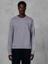 Alpinestars Essentials Ageless Crew, srebrna bluza z okrągłym dekoltem prezentowana na modelu, z małym czarnym logo gwiazdy na piersi, swobodny krój ze ściągaczami przy mankietach i na dole, codzienna odzież uliczna w stylu motorsport