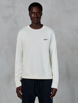 Alpinestars Essentials Ageless Crew, bluza z okrągłym dekoltem w kolorze Off White, małe czarne logo Astars na lewej piersi, codzienna sportowa odzież lifestyle, wysokiej jakości tekstura polaru, noszona przez modela z czarnymi joggerami