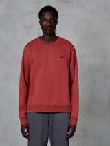 Alpinestars Essentials Ageless Crew, bluza typu crewneck, ceglasta czerwień, małe czarne logo na piersi, model w szarych spodniach, wysokiej jakości miękki polar, styl streetwear