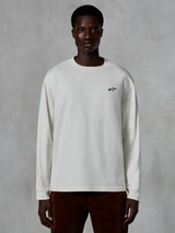 Alpinestars Essentials Ageless LS Tee, koszulka z długim rękawem, kolor złamanej bieli, małe czarne logo gwiazdy na piersi, luźny krój, styl casual streetwear, prezentowana na modelu