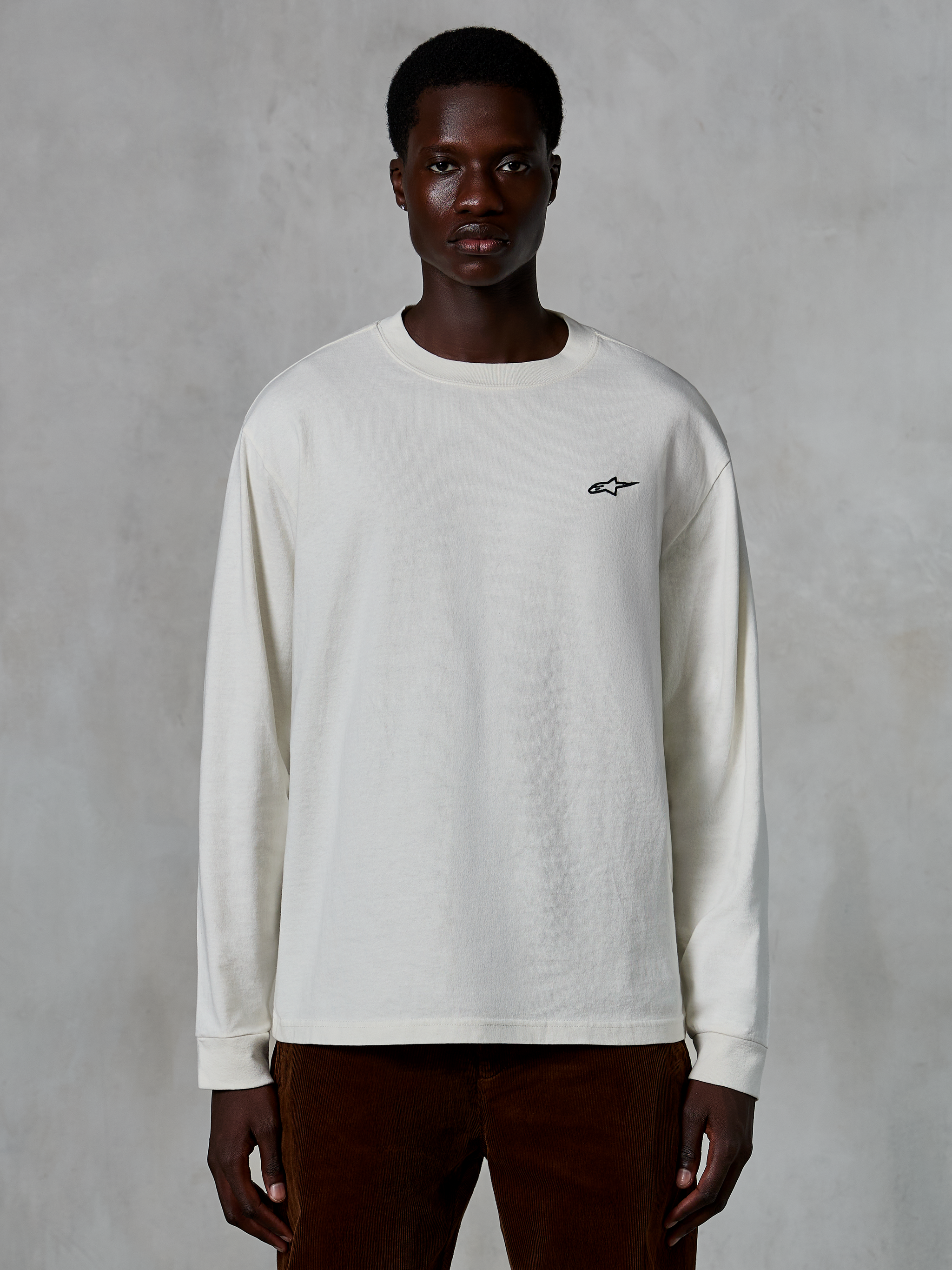 Alpinestars Essentials Ageless LS Tee, koszulka z długim rękawem, kolor złamanej bieli, małe czarne logo gwiazdy na piersi, luźny krój, styl casual streetwear, prezentowana na modelu