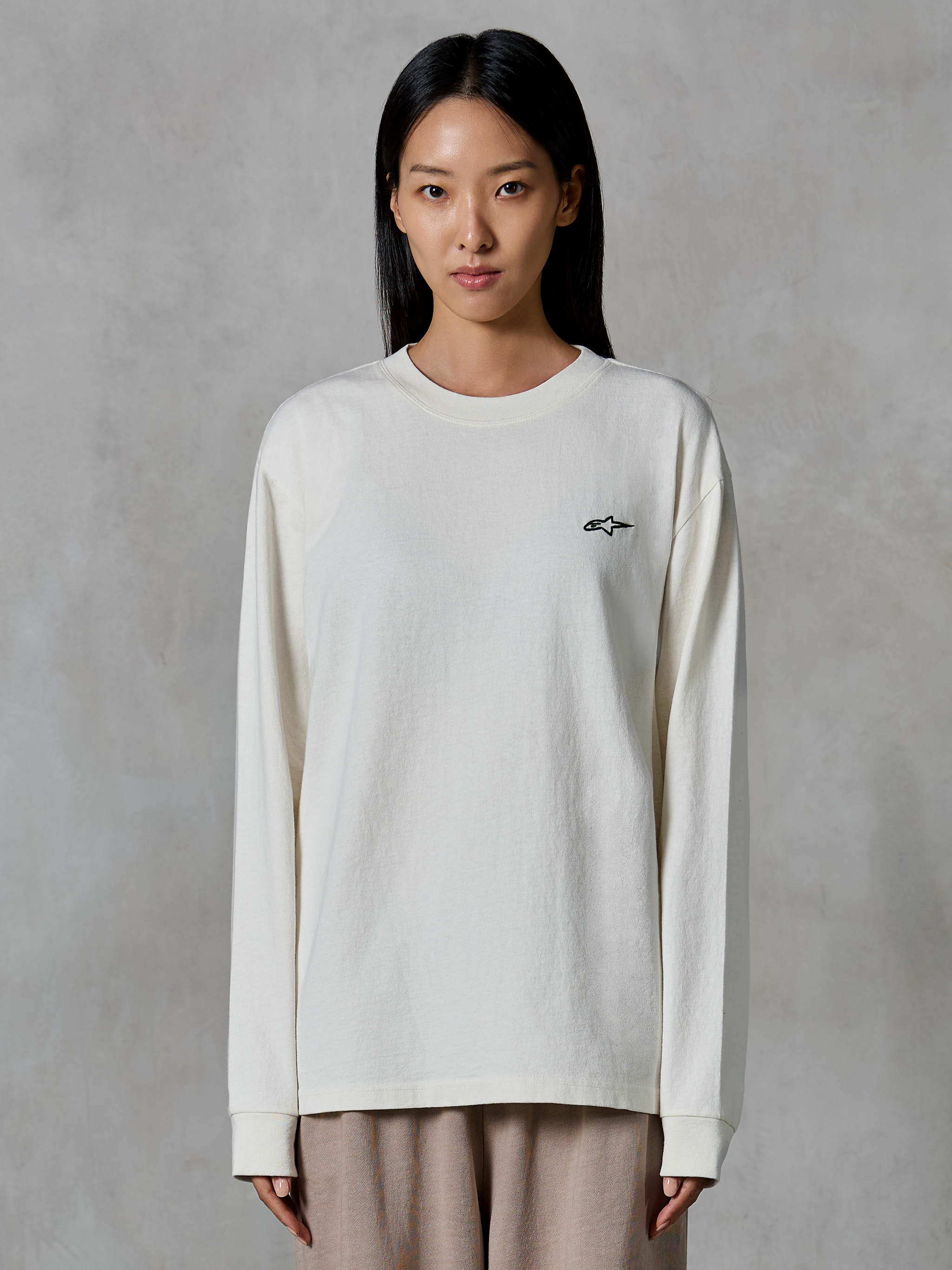 Alpinestars Essentials Ageless LS Tee, koszulka z długim rękawem, kolor złamanej bieli, z małym czarnym logo gwiazdy na piersi, luźny nowoczesny krój, dżersej z bawełny organicznej, codzienny streetwear inspirowany sportami motorowymi