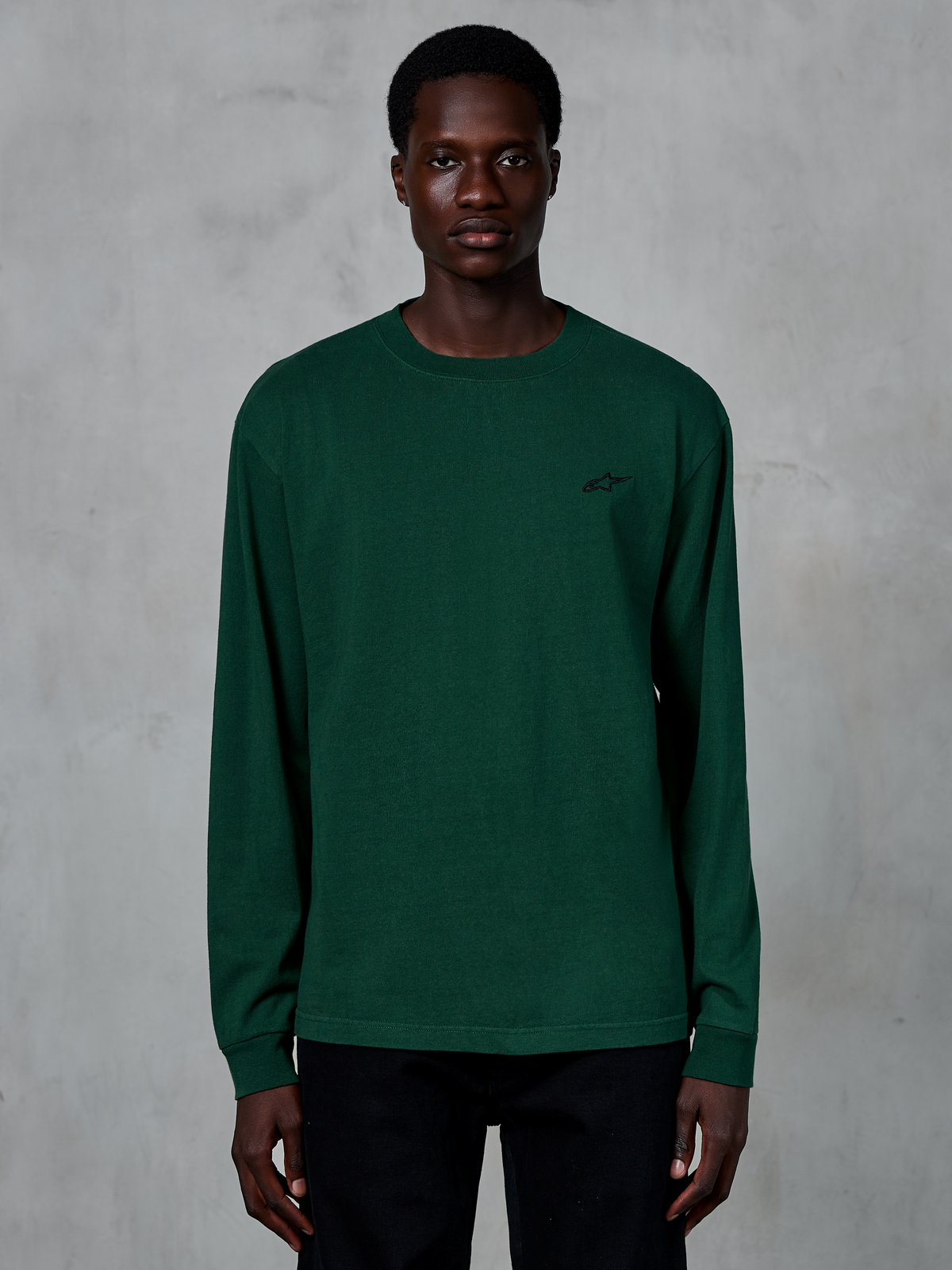 Alpinestars Essentials Ageless LS Tee, koszulka z długim rękawem w kolorze sosnowej zieleni (Pine Green), prezentowana na modelu, małe czarne logo na piersi, casualowy styl streetwear, 100% bawełna organiczna z wykończeniem stone wash