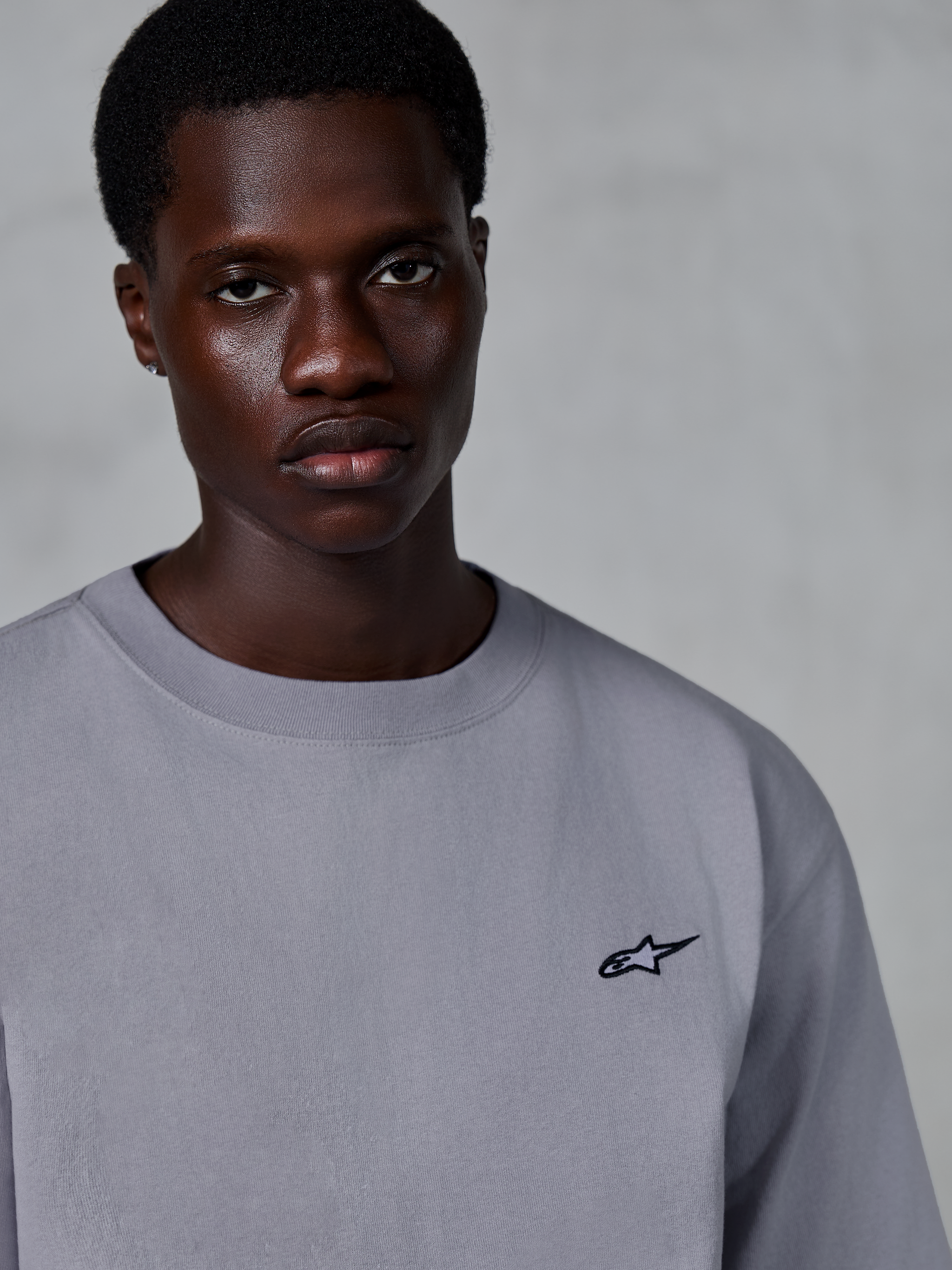 Alpinestars Essentials Ageless SS Tee, koszulka z krótkim rękawem, srebrna, z małym czarnym logo gwiazdy na piersi, prezentowana przez modela, codzienny styl streetwear