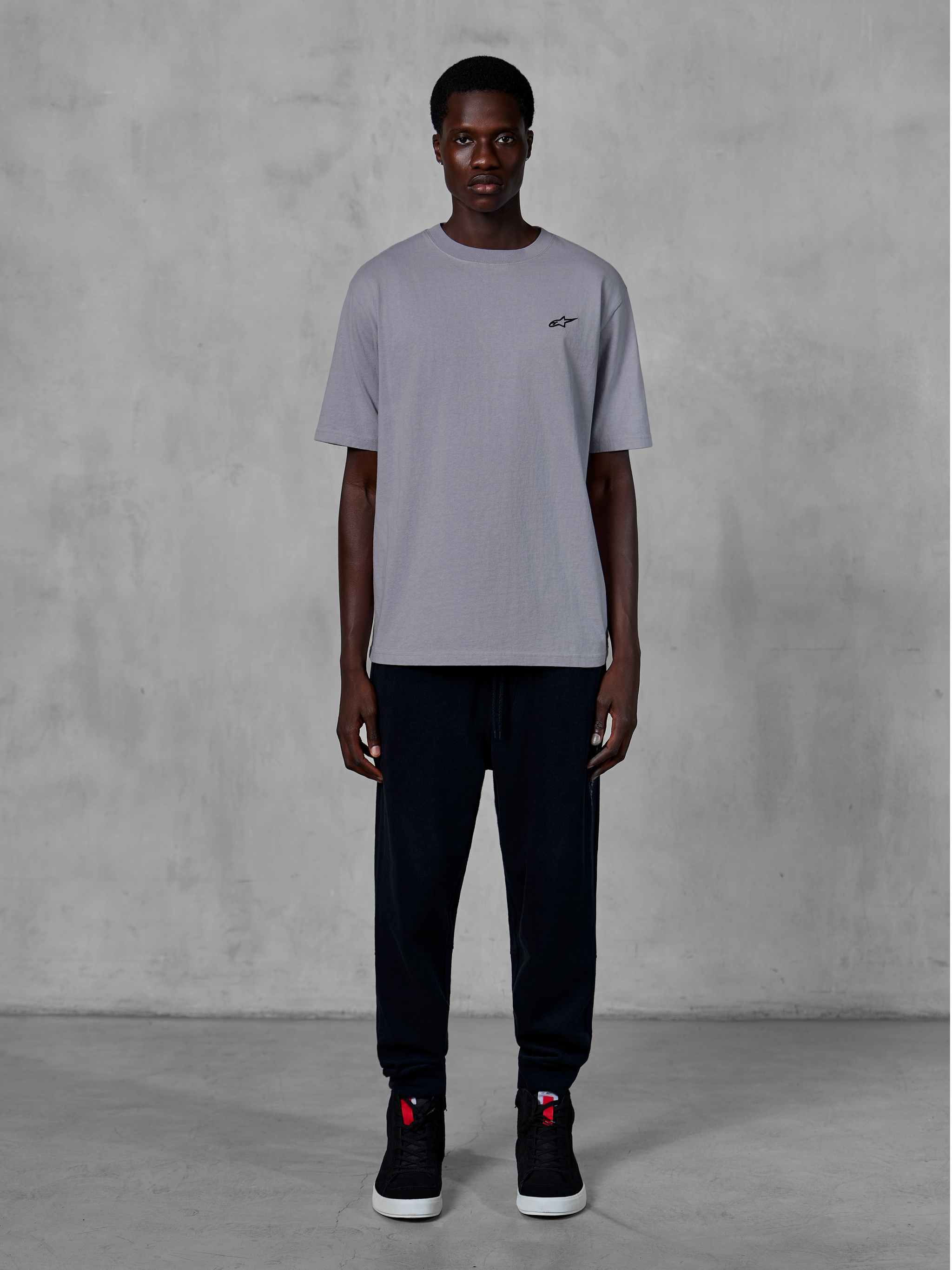 Alpinestars Essentials Ageless SS Tee, koszulka z krótkim rękawem, srebrna, z małym czarnym logo na piersi, zestawiona z czarnymi joggerami i sneakersami, codzienna odzież uliczna w stylu motorsport