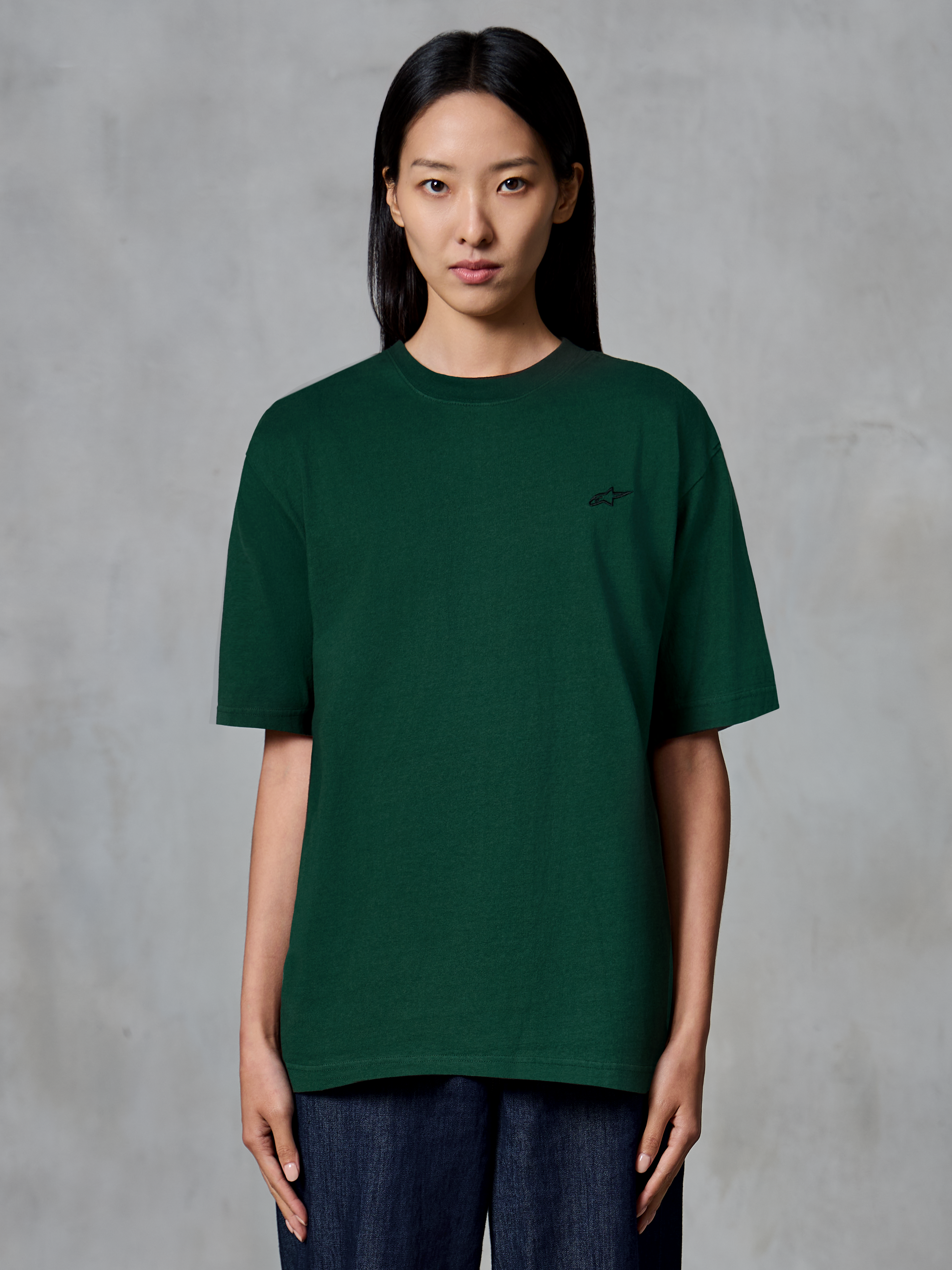 Alpinestars Essentials Ageless SS Tee, koszulka z krótkim rękawem, kolor Pine Green, prezentowana na modelce, małe czarne logo na piersi, luźny krój, bawełna organiczna, casualowy streetwear