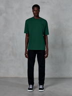 Alpinestars Essentials Ageless SS Tee, koszulka z krótkim rękawem, kolor Pine Green, z subtelnym czarnym logo na piersi, noszona przez modela w czarnych spodniach i sneakersach, casualowy styl streetwear o luźnym kroju