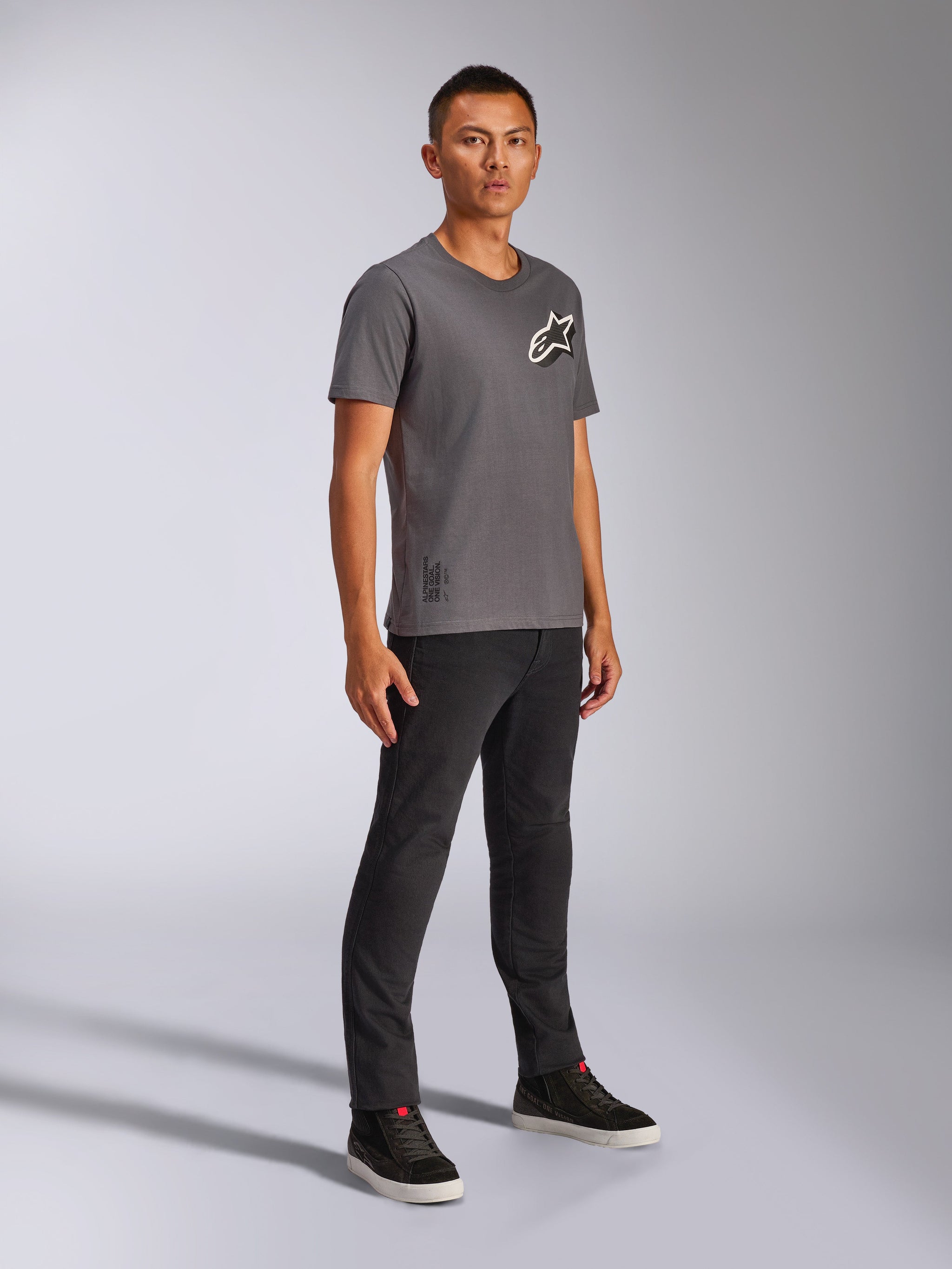 Alpinestars Shaded CSF Tee, Short Sleeve T-Shirt, Charcoal, worn by a male model with black pants and dark sneakers, featuring a slanted white and black Astars logo, casual motorsport-inspired streetwear
