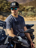 Alpinestars Waving CSF Tee, koszulka z krótkim rękawem, grafitowa, z czarną grafiką powiewającej flagi na piersi, noszona przez mężczyznę siedzącego na motocyklu w słonecznym plenerze, codzienny motocyklowy styl życia