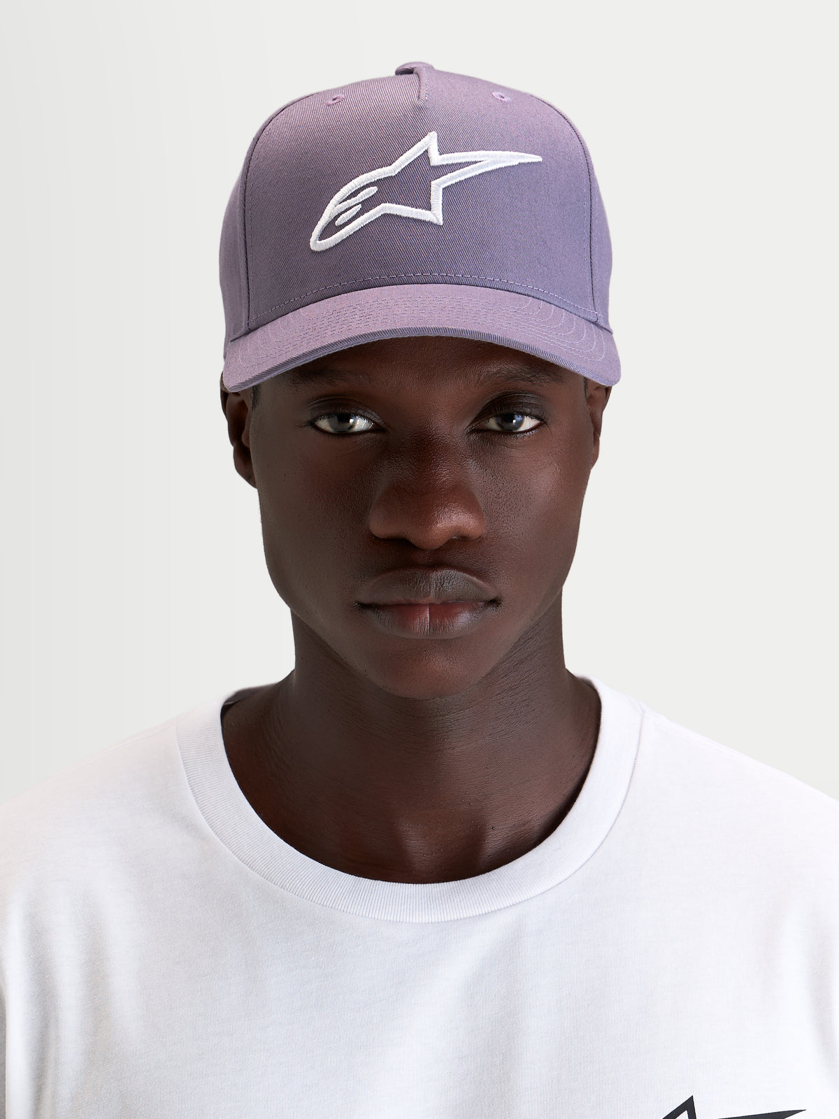 Alpinestars Ageless Snapback Hat, curved bill sportswear cap, dusty purple and white, worn by a model showcasing the front embroidered 3D Astars logo and structured twill profile