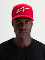 Alpinestars Ageless Snapback, czerwona czapka z daszkiem noszona przez modela, z białym wypukłym haftem 3D z logo Astars, zakrzywionym daszkiem i usztywnioną koroną z bawełnianego kepru