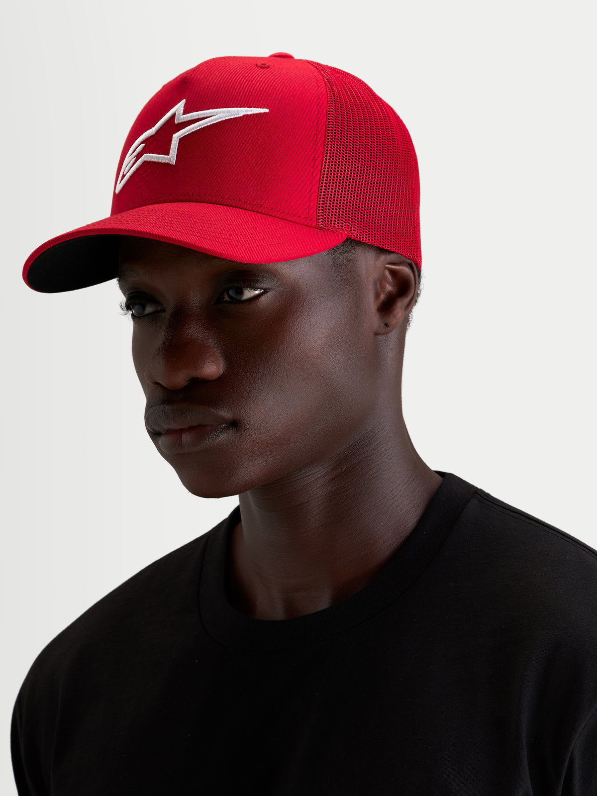 Alpinestars Czapka Ageless Snapback, czerwona czapka z daszkiem noszona przez modela, z wypukłym haftem 3D logo Astars w kolorze białym oraz zakrzywionym daszkiem
