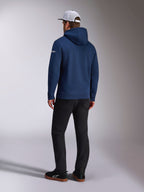Alpinestars Frontal Hoodie, Rear view of a navy blue pullover fleece hoodie, white word logo on the sleeve, paired with black pants and a white mesh trucker hat, casual motorsport-inspired streetwear