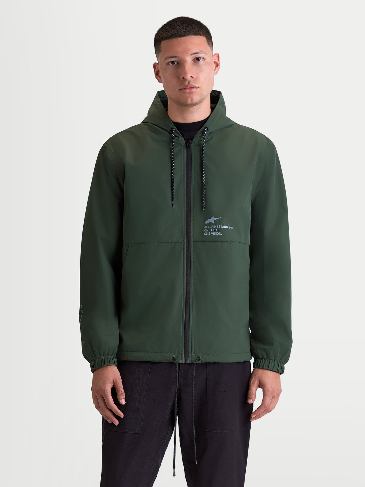 Alpinestars Kurtka Speeder Resolve Ochrona Przed Wiatrem, lekka męska kurtka z kapturem do użytku miejskiego, zielona, siatkowa podszewka, regulowany kaptur ze sznurkiem i pełny zamek błyskawiczny z przodu, logo Alpinestars na piersi, widok z przodu na modelu.