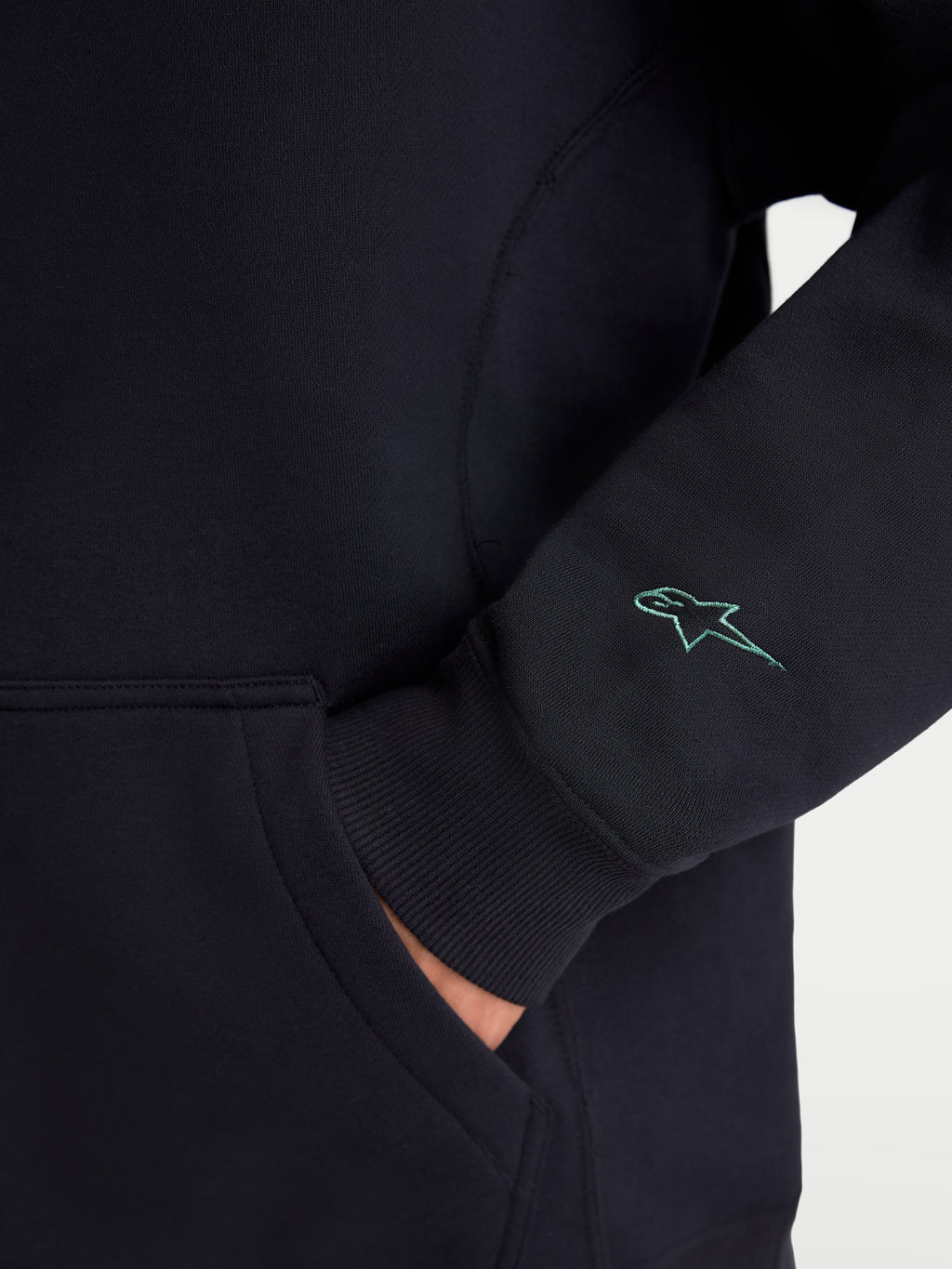 Alpinestars Bluza Guise Oversize, czarna bluza sportowa z polaru, zbliżenie na haftowane logo Astars na rękawie, prążkowany mankiet i detal kieszeni kangurki, mieszanka bawełny i poliestru z recyklingu, swobodny krój oversize.