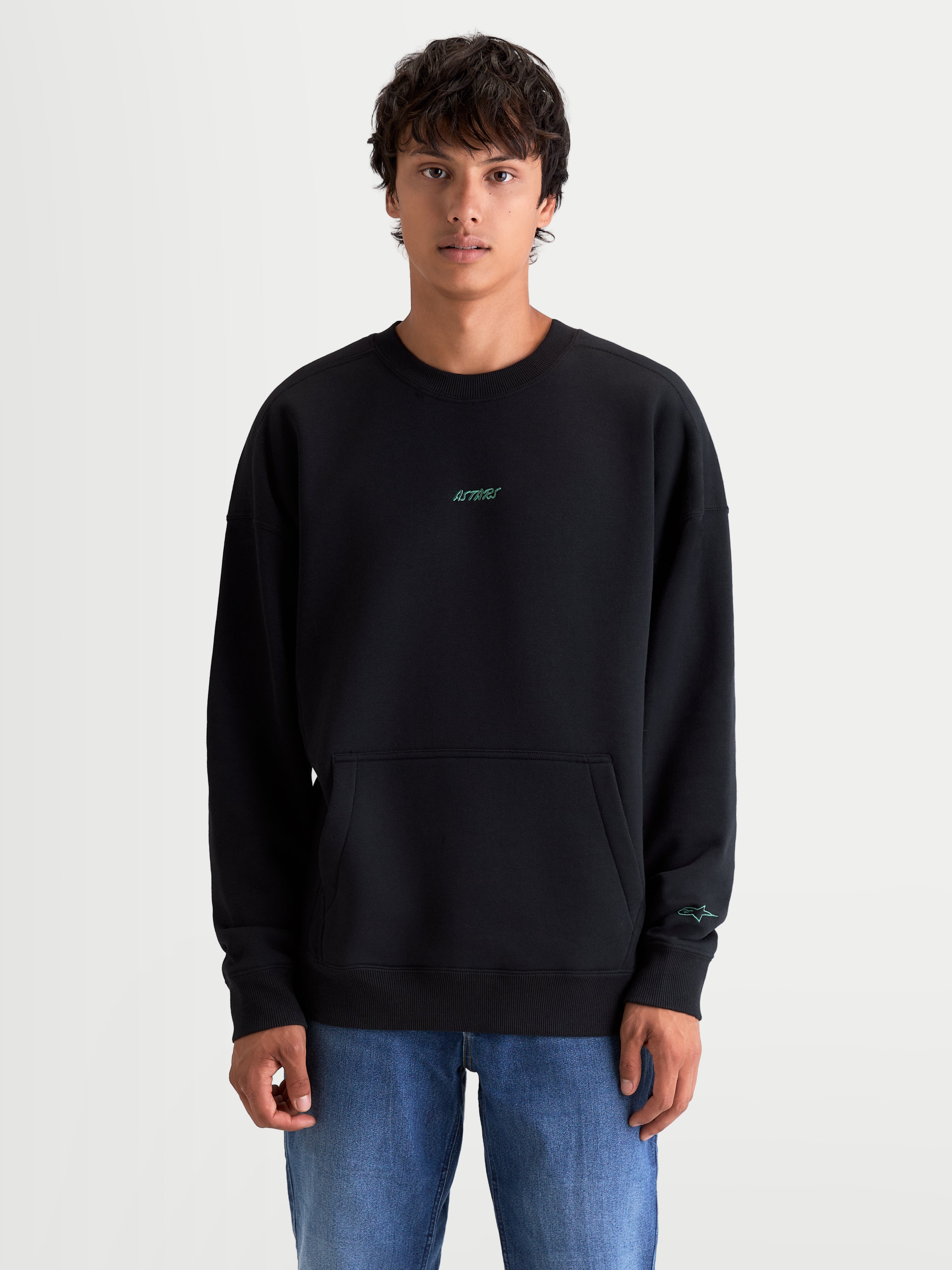 Alpinestars bluza Guise Oversize, czarna bluza dresowa z okrągłym dekoltem prezentowana na modelu, krój oversize z kieszenią kangurką, haftowane logotypy Astars w kolorze morskim na piersi i rękawie, polar z bawełny i poliestru z recyklingu, sportowa odzież codzienna.