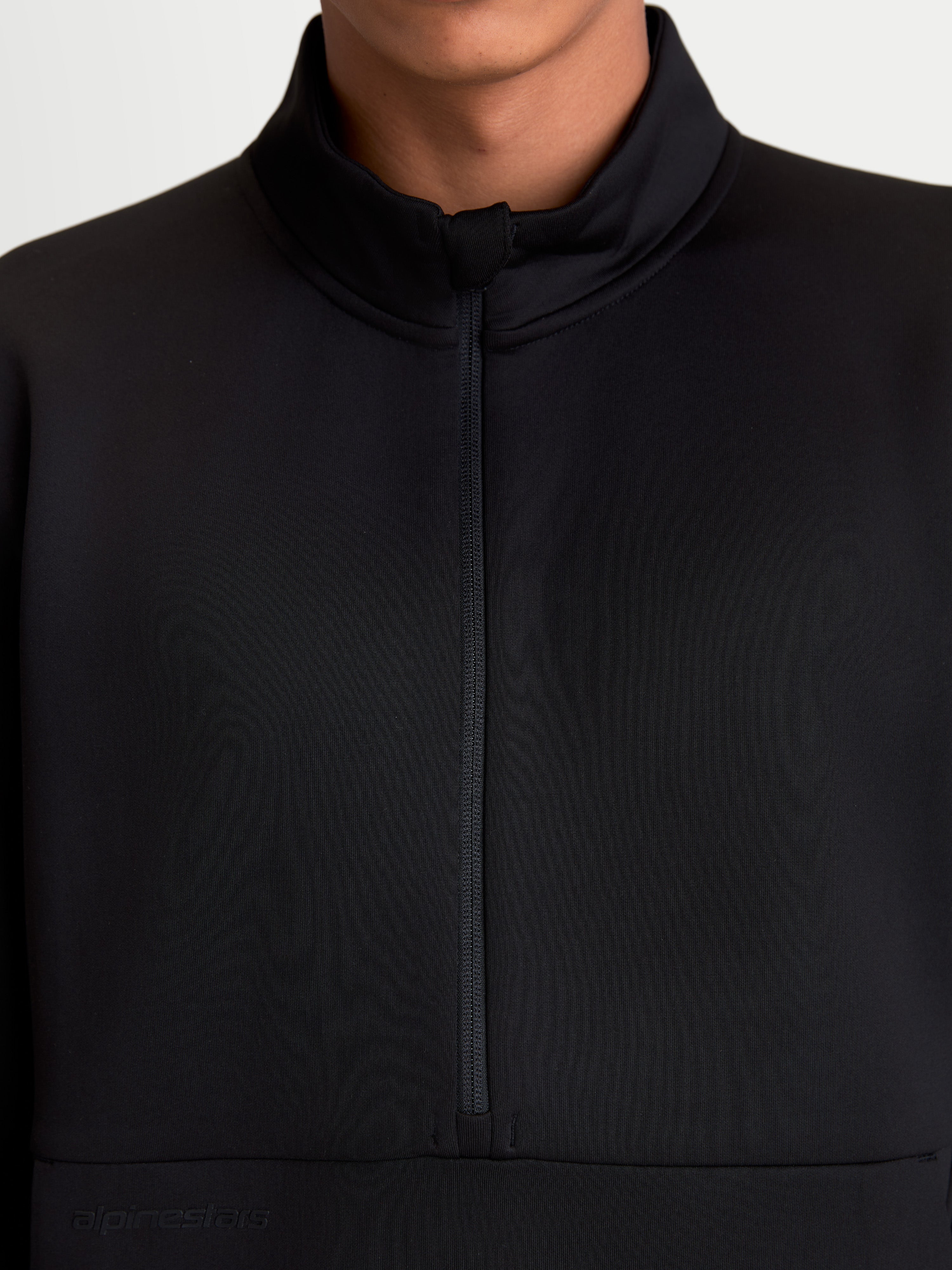 Alpinestars Bluza Apera Half-Zip, czarna bluza sportowa typu pullover, zbliżenie na zapięcie na suwak do połowy i wysoki kołnierz, widok na modelu, wykonana z polaru tri-blend z tonalnym logo Alpinestars, nowoczesny wygląd inspirowany motorsportem.
