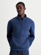 Alpinestars bluza Apera Half-Zip prezentowana na modelu, męska bluza sportowa z zamkiem do połowy i kieszenią kangurką, kolor stalowy niebieski, tonalne logo Alpinestars, wykonana z dwustronnego polaru tri-blend, styl casualowy inspirowany motorsportem