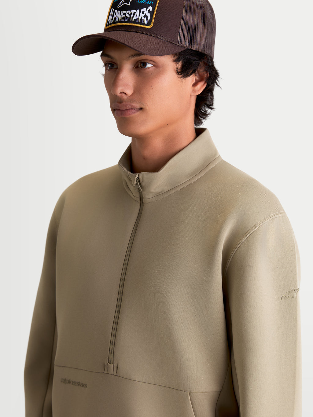 Alpinestars bluza Apera z półzamkiem, beżowa męska bluza sportswear, dwustronny polar tri-blend, zapięcie na półzamek i tonalne logo, casualowa odzież inspirowana motorsportem do codziennego noszenia prezentowana na modelu.
