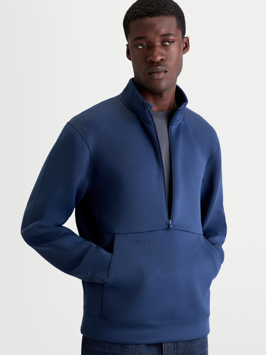 Alpinestars bluza Apera Half-Zip, męska bluza sportowa z kapturem, niebieska, zapięcie na zamek do połowy, kieszeń kangurka z tonalnym logo, model prezentujący casualową odzież motorsportową.