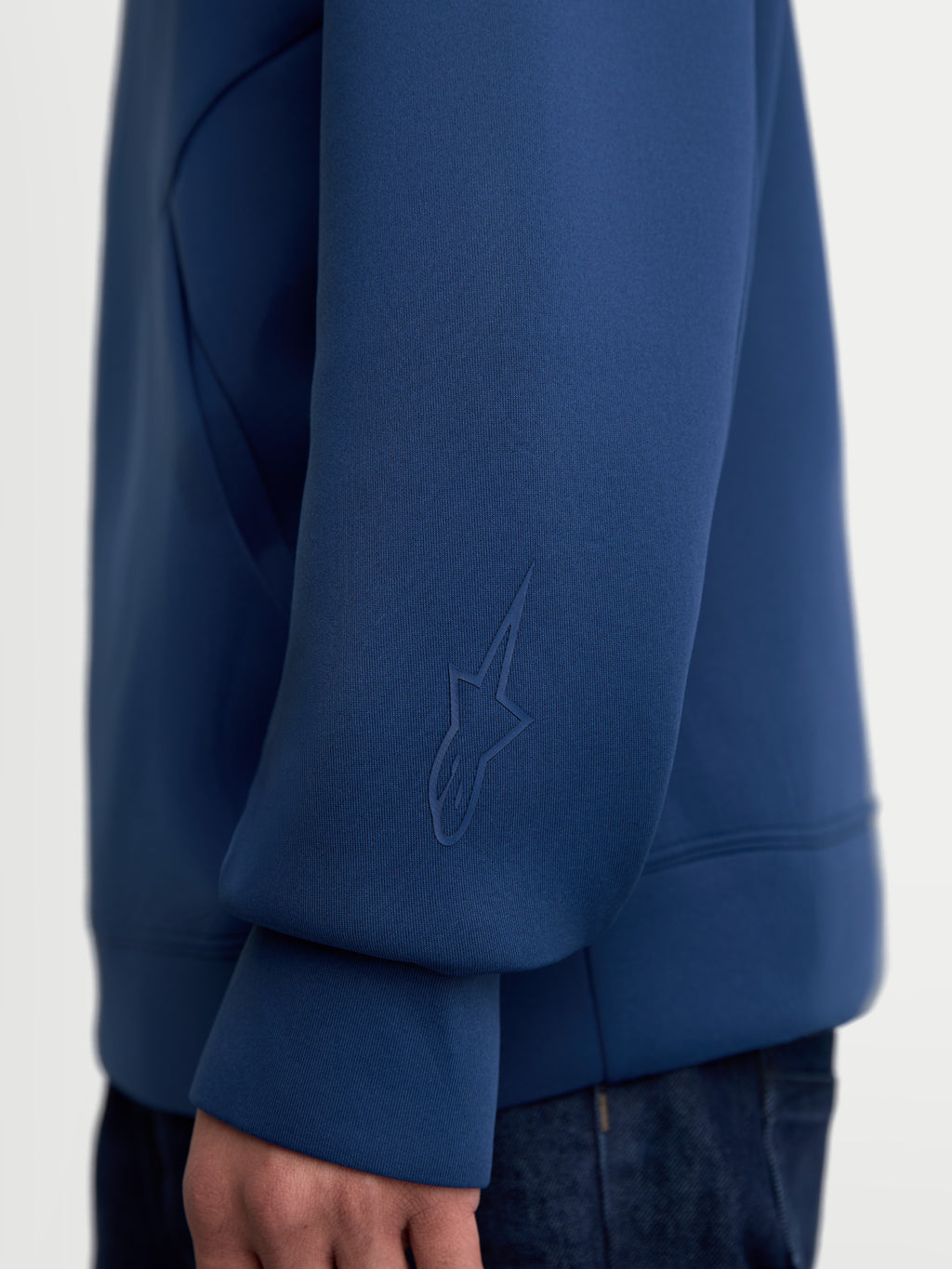 Alpinestars Bluza Z Kapturem Datrix, niebieska bluza sportowa premium, zbliżenie na rękaw z tonalnym logo HD Alpinestars, wykonana z miękkiego dwustronnego polaru, casualowa odzież codzienna w stylu motorsport.