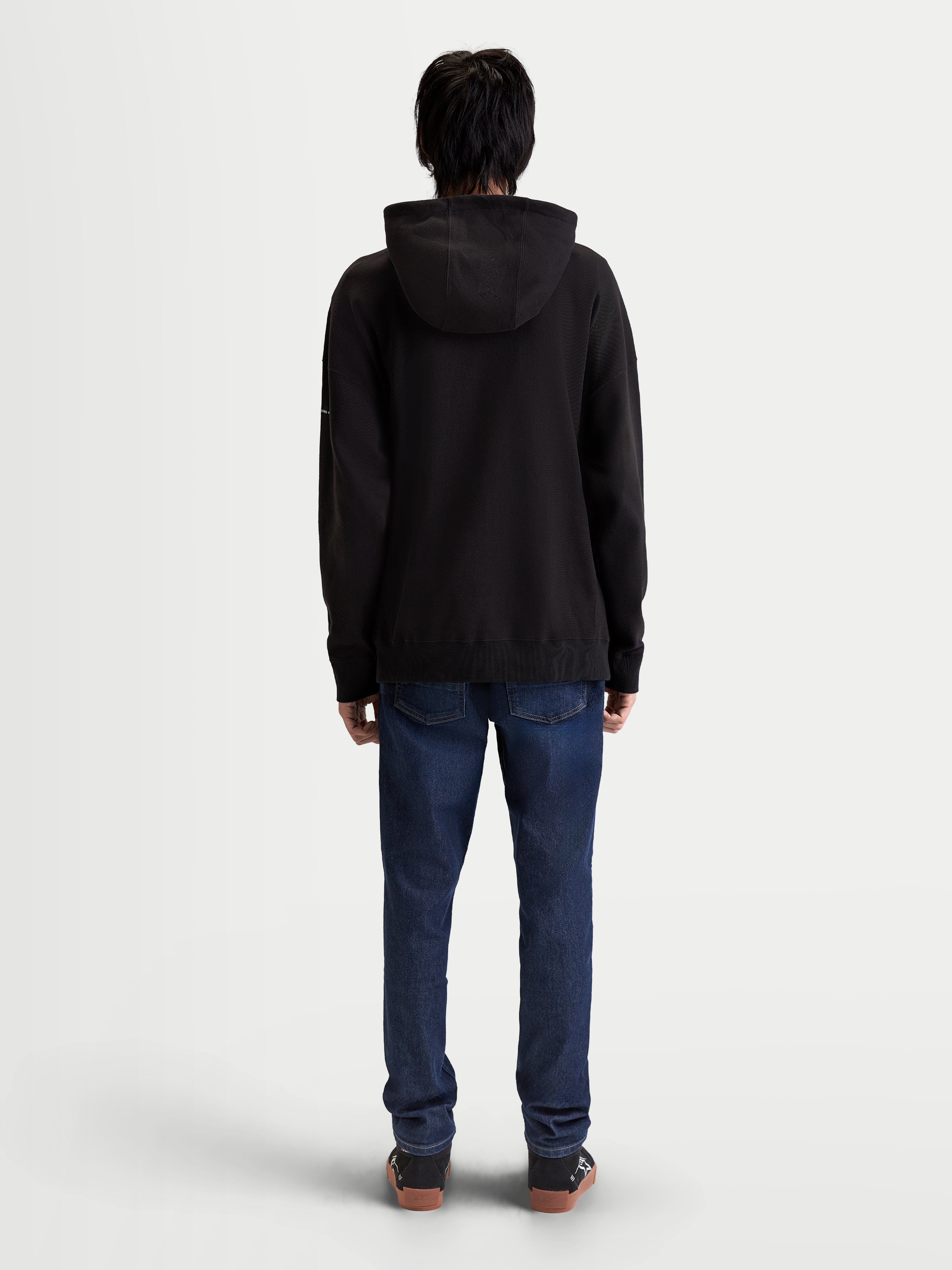 Alpinestars Camino Textured Oversized Hoodie, czarna bluza z kapturem premium, teksturowany polar dzianinowy o splocie twill, luźny krój, widok z tyłu na modelu, sportowa odzież lifestyle