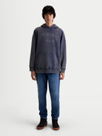 Alpinestars bluza z kapturem Infinite Washed Oversized, casualowa bluza sportowa typu pullover noszona przez modela, granatowa z wykończeniem snow-wash, kieszeń kangurka i haftowany napis Alpinestars na klatce piersiowej, bawełna premium i poliester z recyklingu, krój oversize zapewniający komfort.