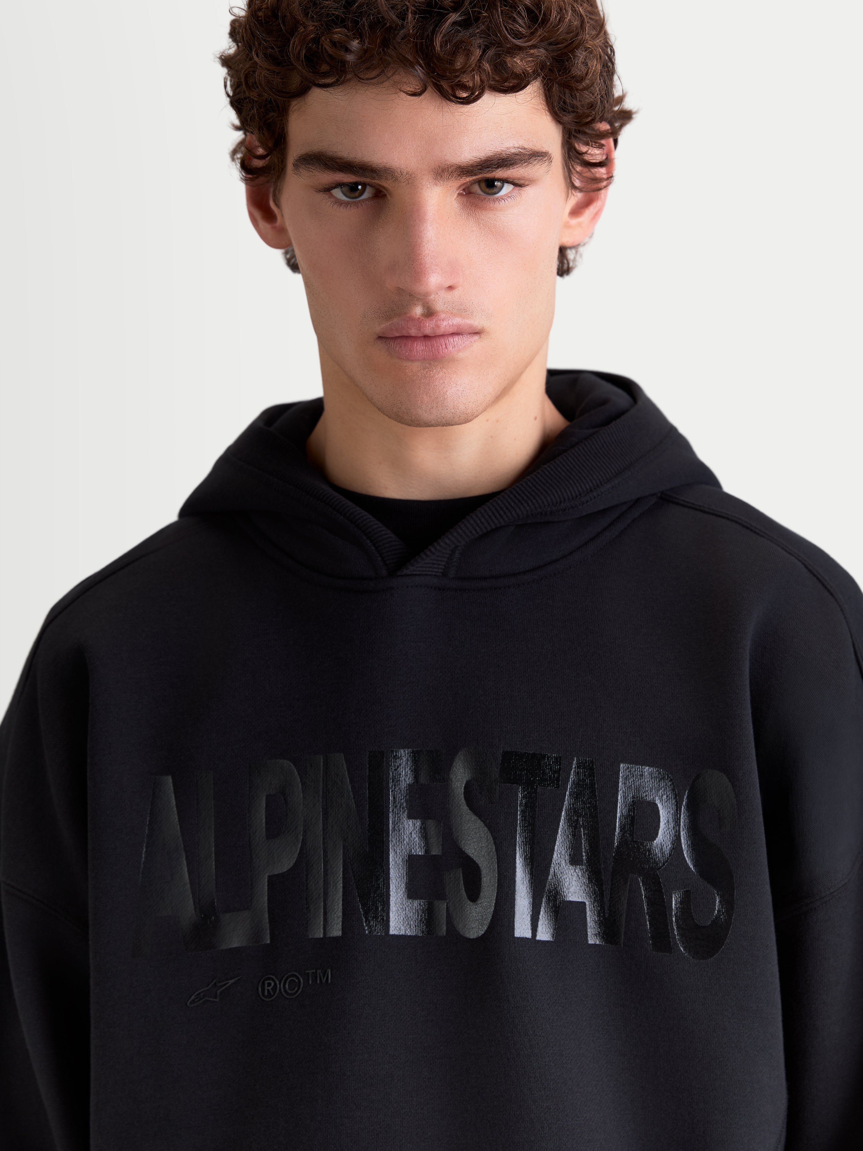 Alpinestars bluza z kapturem Shaw Oversized, czarna męska bluza sportowa o luźnym kroju, teksturowane tonalne logo Alpinestars na klatce piersiowej, miękki bawełniany polar, na modelu