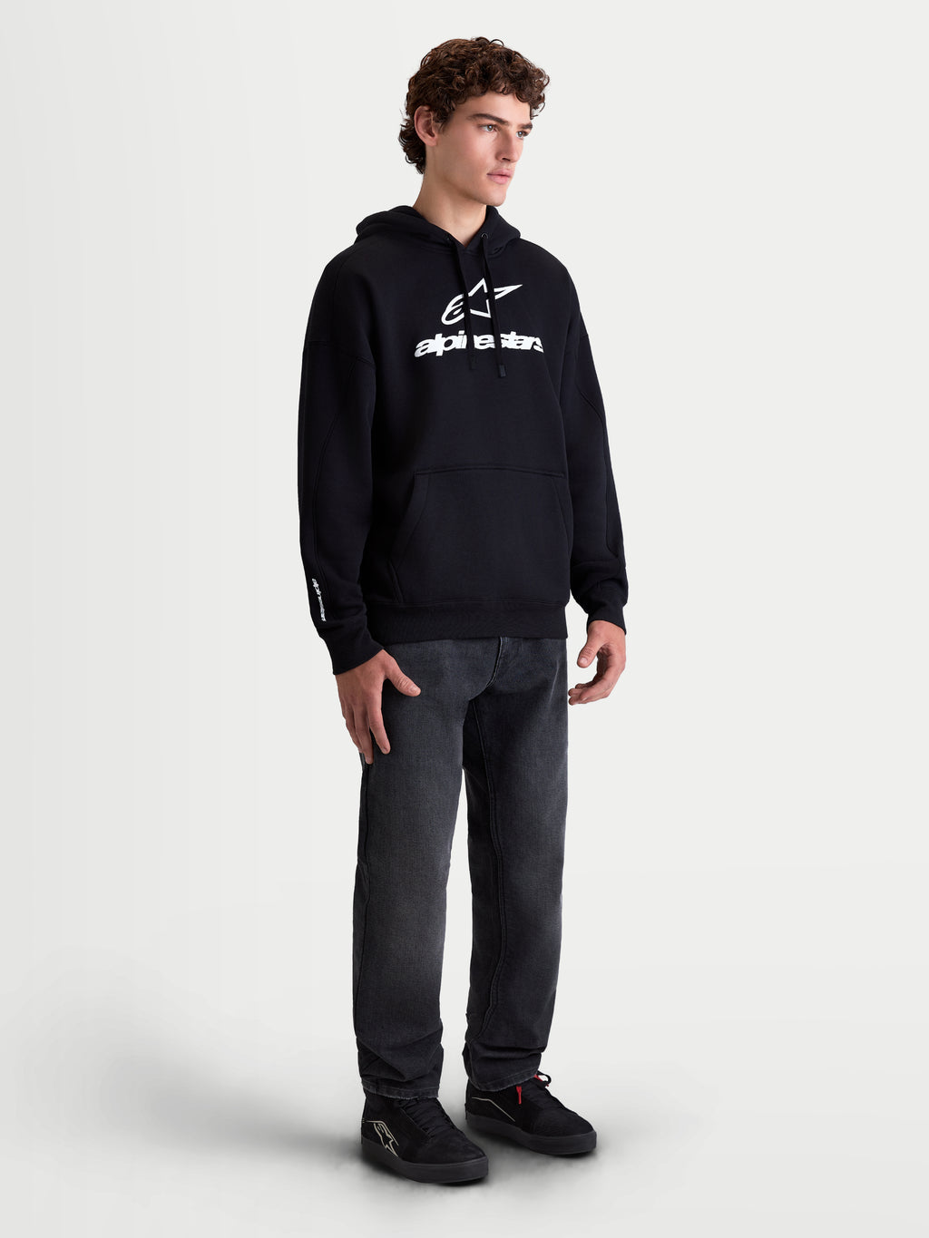 Alpinestars bluza z kapturem Prelude Oversized, męska bluza sportowa, czarna z białym wypukłym logo, luźny krój oversize i kieszeń kangurka, prezentowana na modelu.