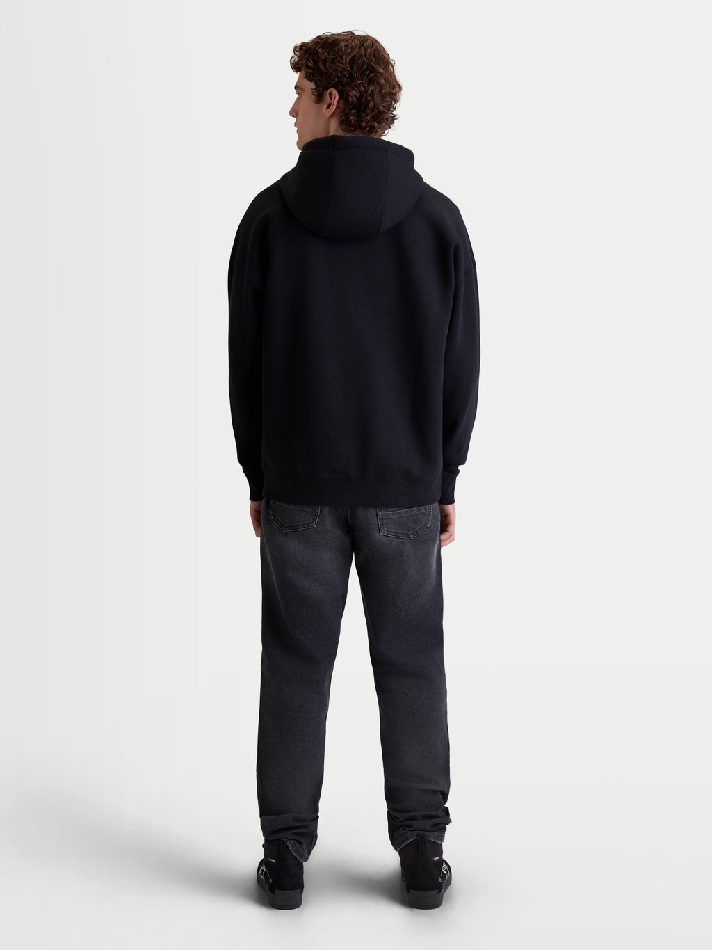 Alpinestars bluza z kapturem Prelude Oversized, sportowa bluza z polarem, czarna, luźny fason oversize, widok z tyłu na modelu, obniżone ramiona i prążkowany ściągacz, mieszanka bawełny premium, codzienna odzież sportowa.