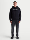 Alpinestars bluza z kapturem Race Wordmark na modelu, czarna i biała bluza sportowa typu pullover z kapturem, białe logo Race Linear Word na klatce piersiowej i grafika Ageless na rękawie, produkt unisex, mieszanka bawełny i poliestru z recyklingu, casualowy styl motorsportowy.