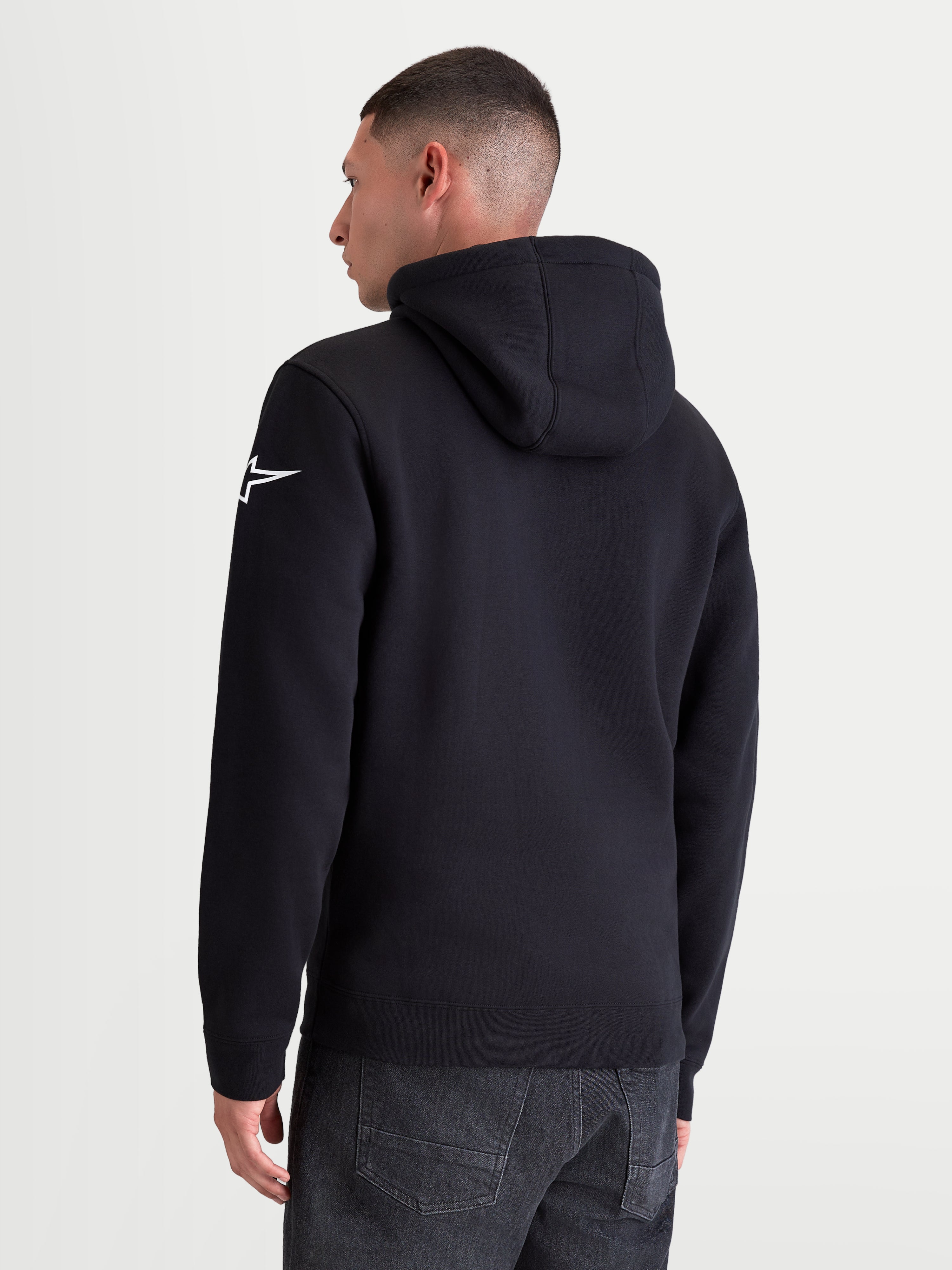 Alpinestars Bluza Z Kapturem Race Wordmark, czarna bluza z kapturem, widok z tyłu na modelu, białe logo Ageless star na lewym rękawie, casualowa odzież sportowa inspirowana motorsportem, wykonana z mieszanki bawełny i poliestru z recyklingu.