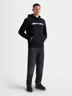 Alpinestars bluza z kapturem Race Wordmark, męska bluza dresowa, czarna, biały linearny logotyp na klatce piersiowej, kaptur z podszewką i sznurkami, przednia kieszeń typu kangurka, casualowa odzież sportowa w stylu motorsport, prezentowana na modelu.