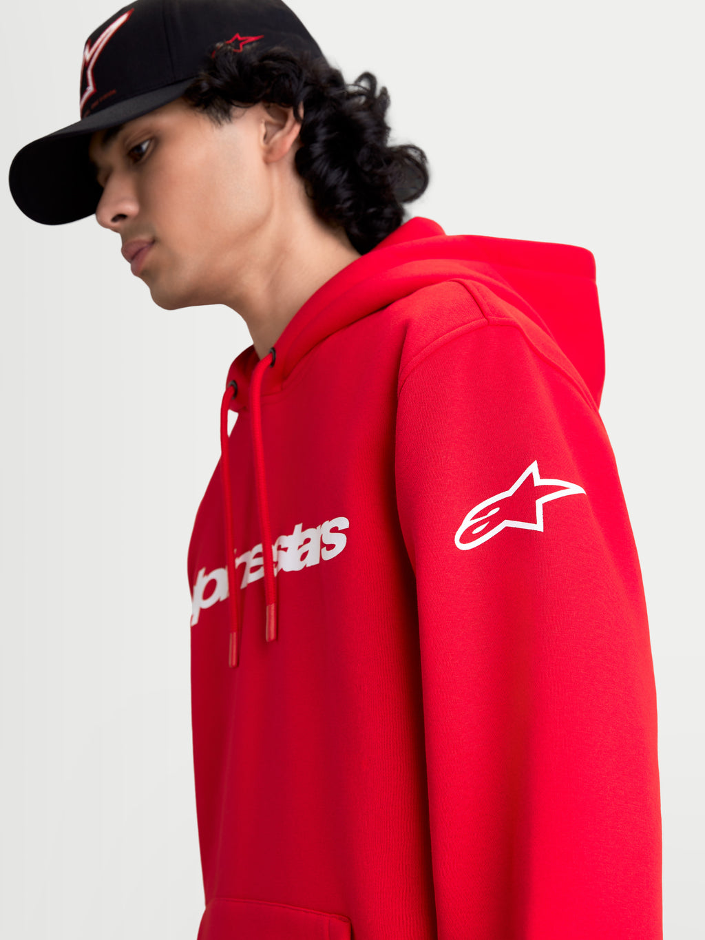 Alpinestars bluza z kapturem Race Wordmark, czerwona i biała sportowa bluza typu polar, widok na modelu z białym logo Ageless na rękawie i brandingiem Race Linear z przodu, casualowy design inspirowany motorsportem.