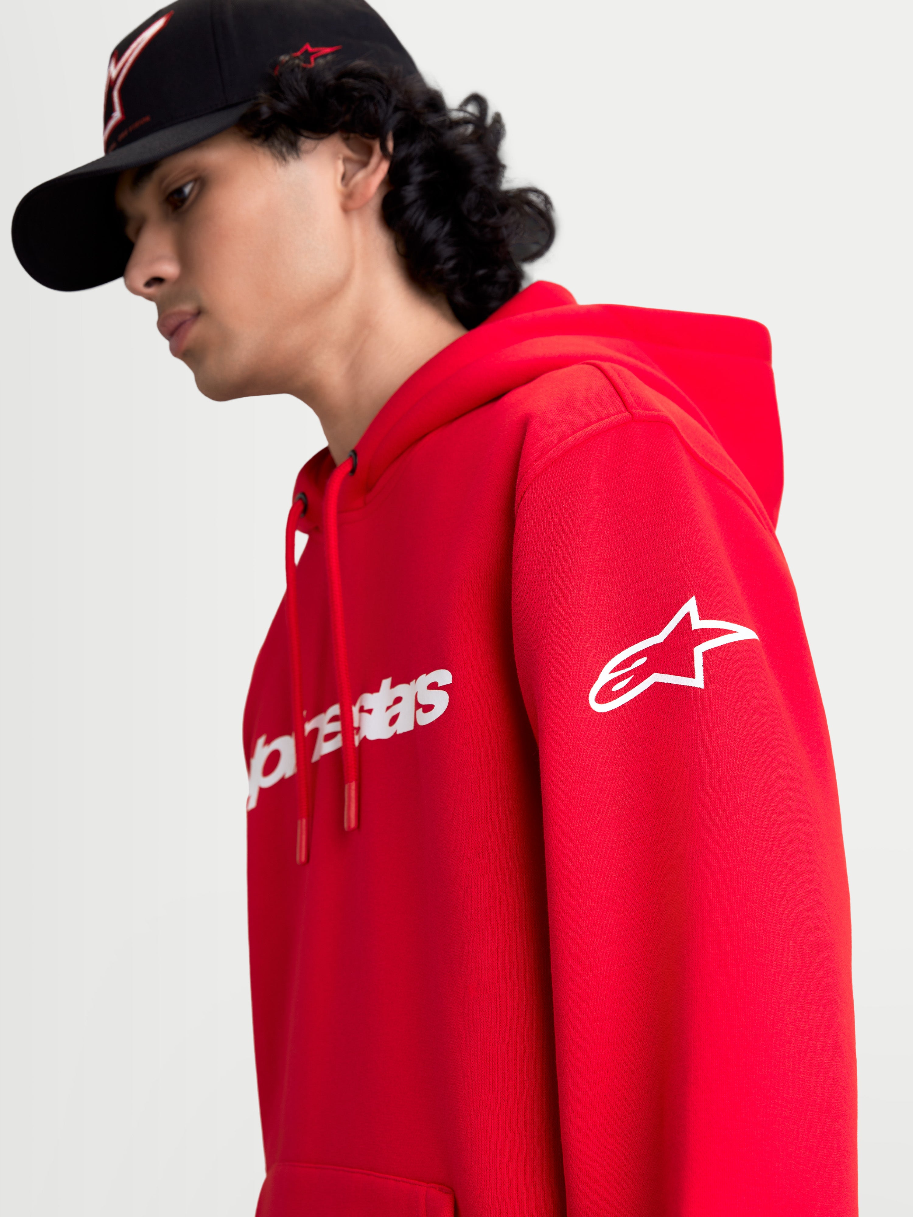 Alpinestars bluza z kapturem Race Wordmark, czerwona i biała sportowa bluza typu polar, widok na modelu z białym logo Ageless na rękawie i brandingiem Race Linear z przodu, casualowy design inspirowany motorsportem.