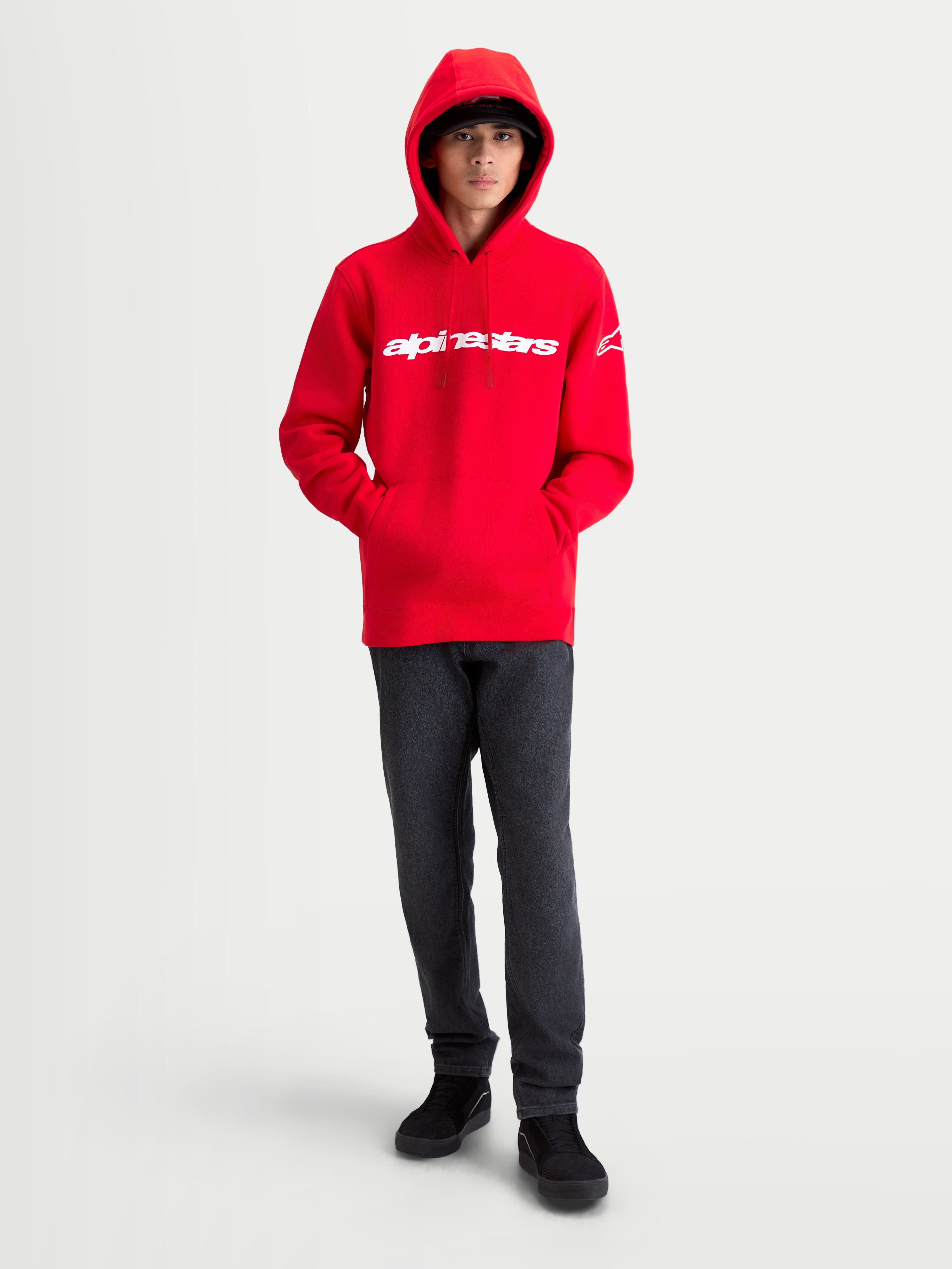 Alpinestars Bluza z kapturem Race Wordmark, męska bluza z polarem, czerwona i biała, wyrazisty liniowy napis na piersi i logo Ageless na rękawie, model w bluzie z założonym kapturem, codzienna odzież inspirowana motorsportem.