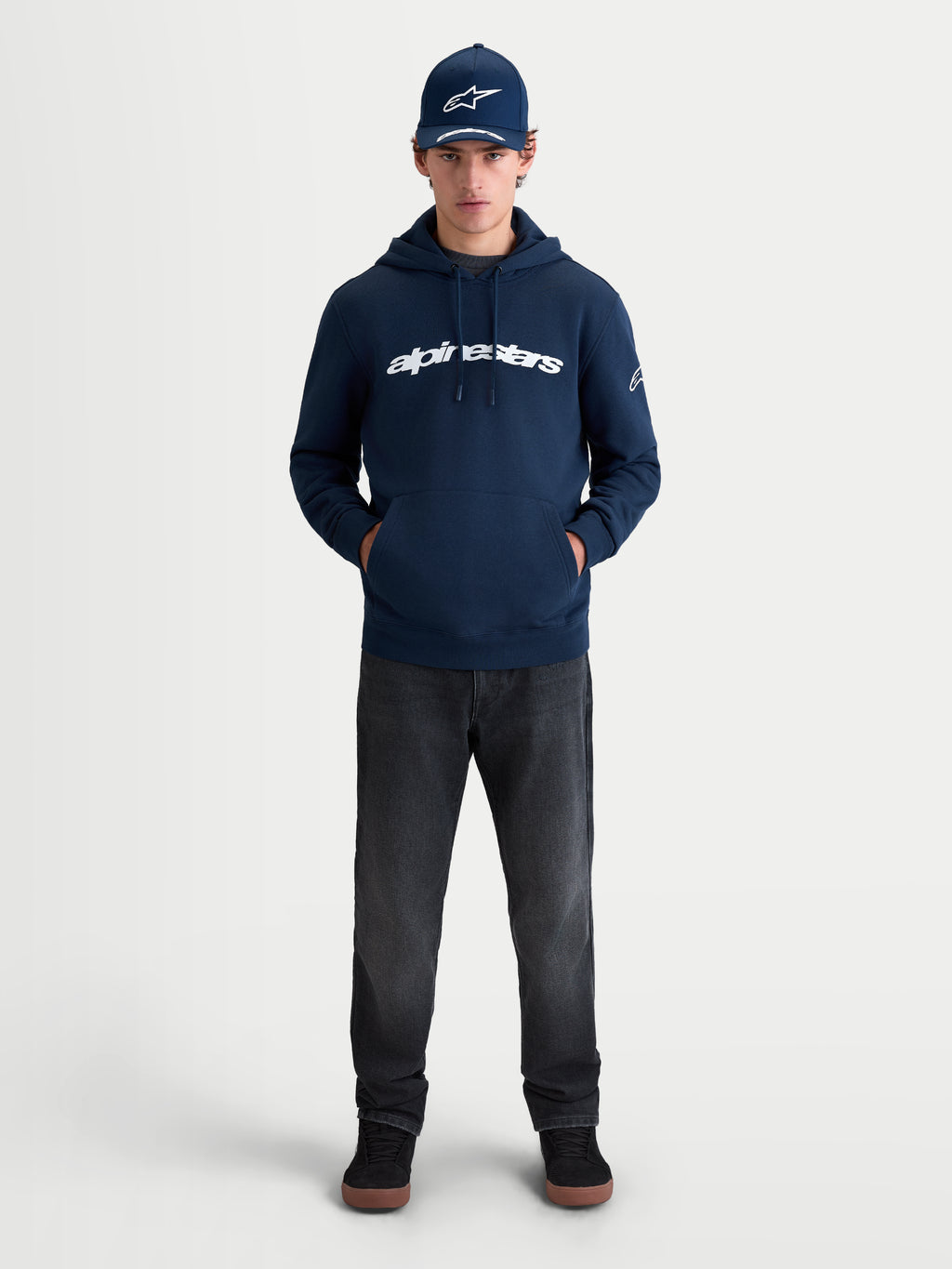 Alpinestars Bluza Z Kapturem Race Wordmark, sportowa męska i damska bluza typu polar, granatowa i biała, wyrazisty napis z przodu i logo Ageless na rękawie, widok lifestyle na modelu, styl motorsportowy.