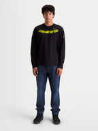 Alpinestars Velocifier CSF Tee, Long Sleeve Sportswear, Black and Yellow, On-Model. This unisex cotton-blend long sleeve t-shirt features a vibrant yellow curved Astars front graphic, matching shoulder logos, and rib cuffs, designed for daily casual wear with a motorsport-inspired aesthetic.