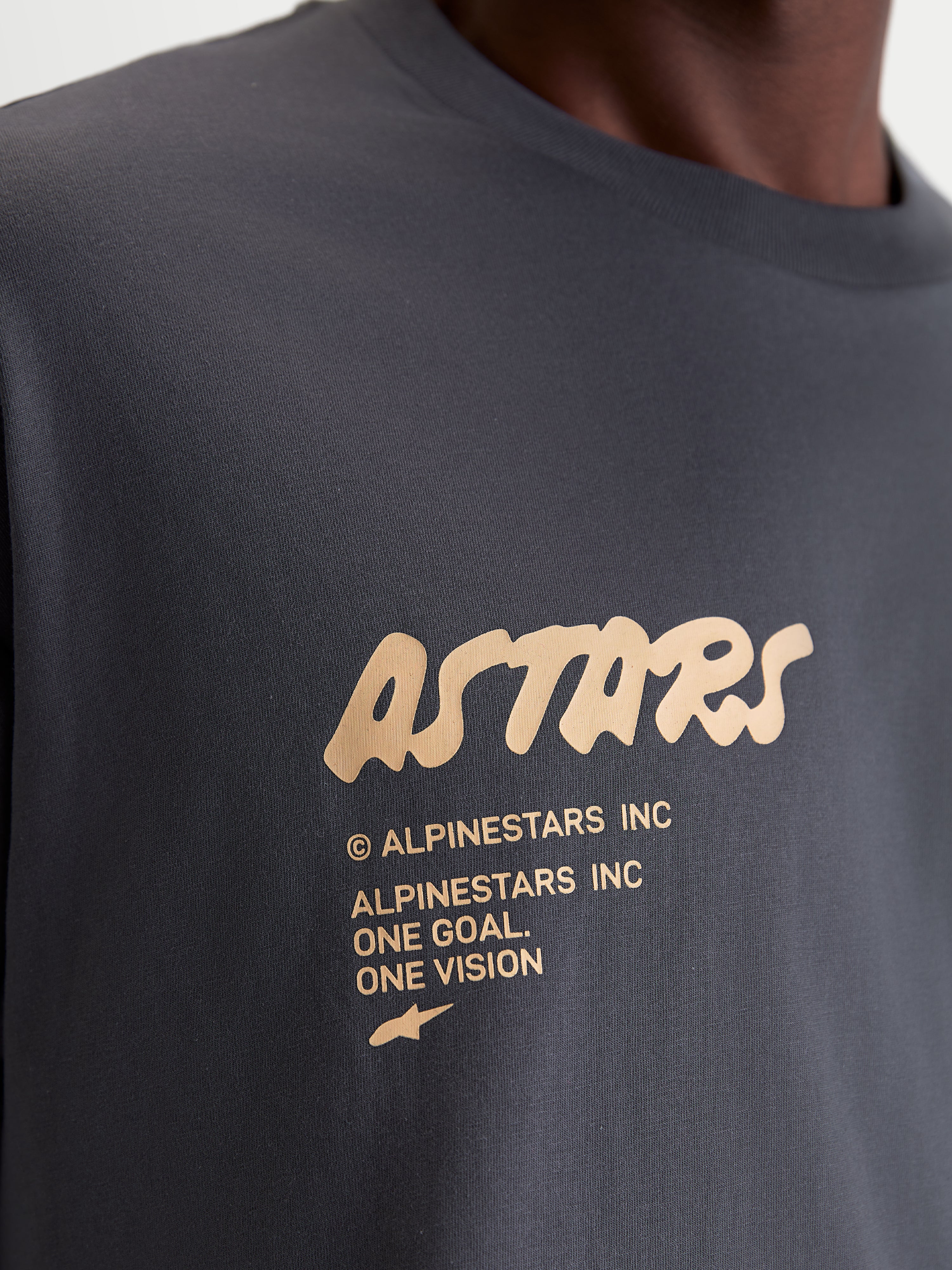 Alpinestars Chalk Oversized CSF Tee, Unisex Sportswear Short Sleeve T-Shirt, Charcoal Gray with Cream Graphic, Close-up detail of front chest logo featuring Astars branding and One Goal One Vision manifesto, premium cotton-poly blend.