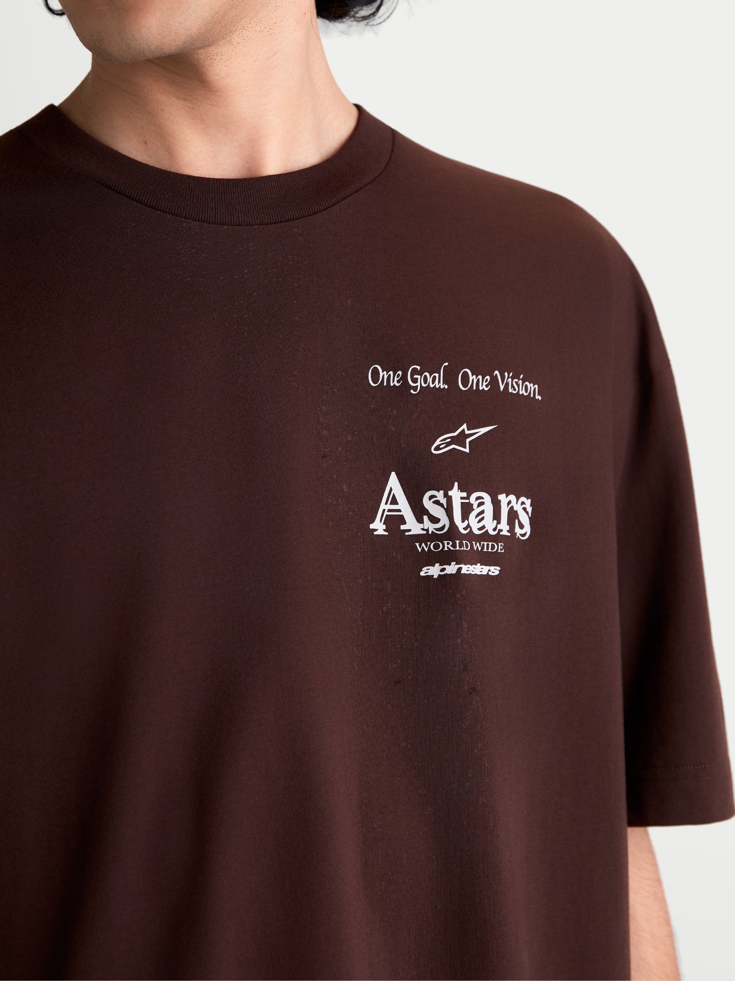 Alpinestars Koszulka Post Oversized CSF, brązowa koszulka z krótkim rękawem sportswear, zbliżenie na białą grafikę na klatce piersiowej z napisem One Goal. One Vision. i logo Astars worldwide, wykonana z miękkiej mieszanki bawełny i poliestru.
