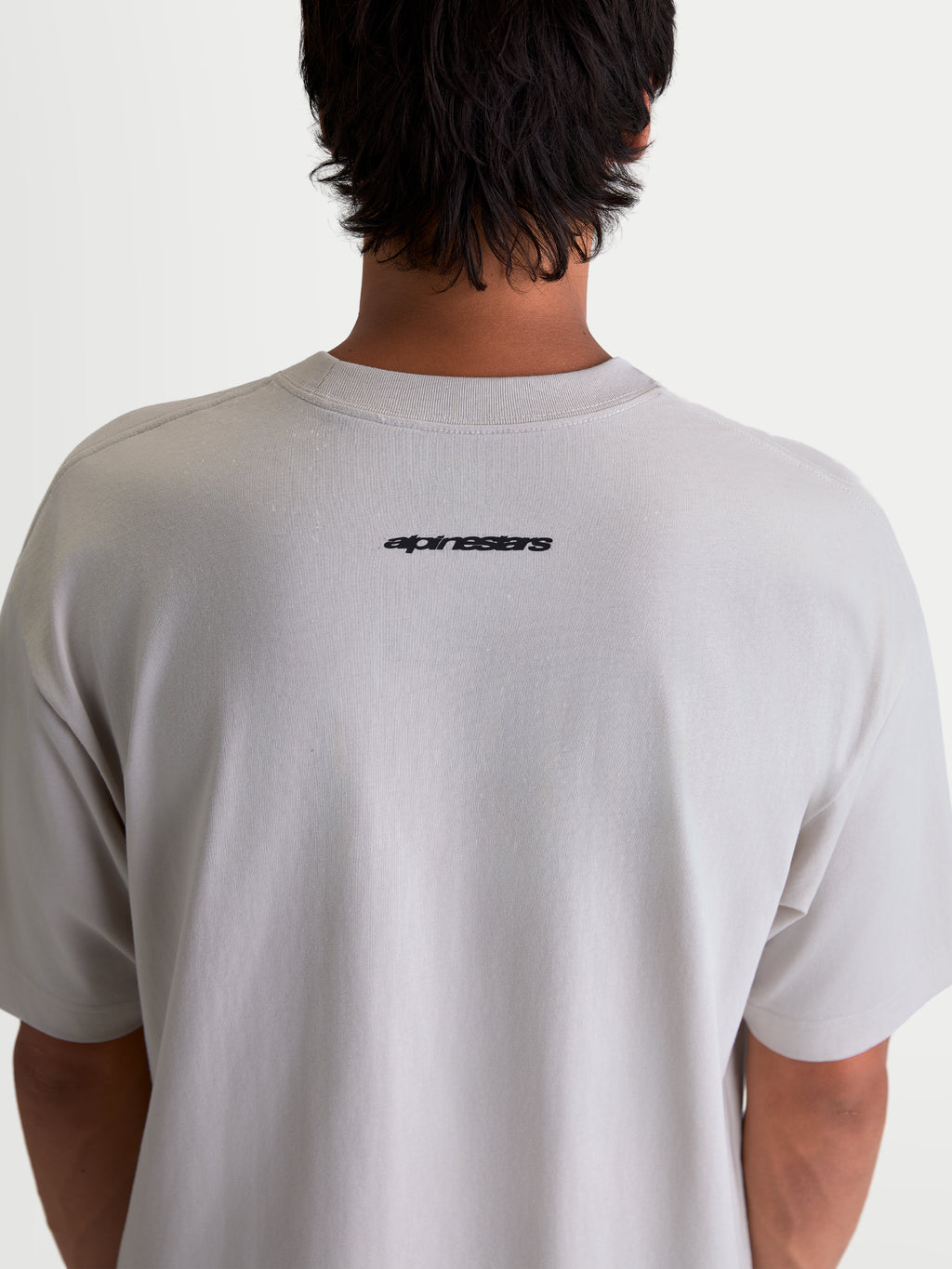 Alpinestars Mandate Oversized CSF, szara koszulka z krótkim rękawem, czarny logotyp Alpinestars na górze pleców, krój oversize na modelu, codzienna odzież sportowa.