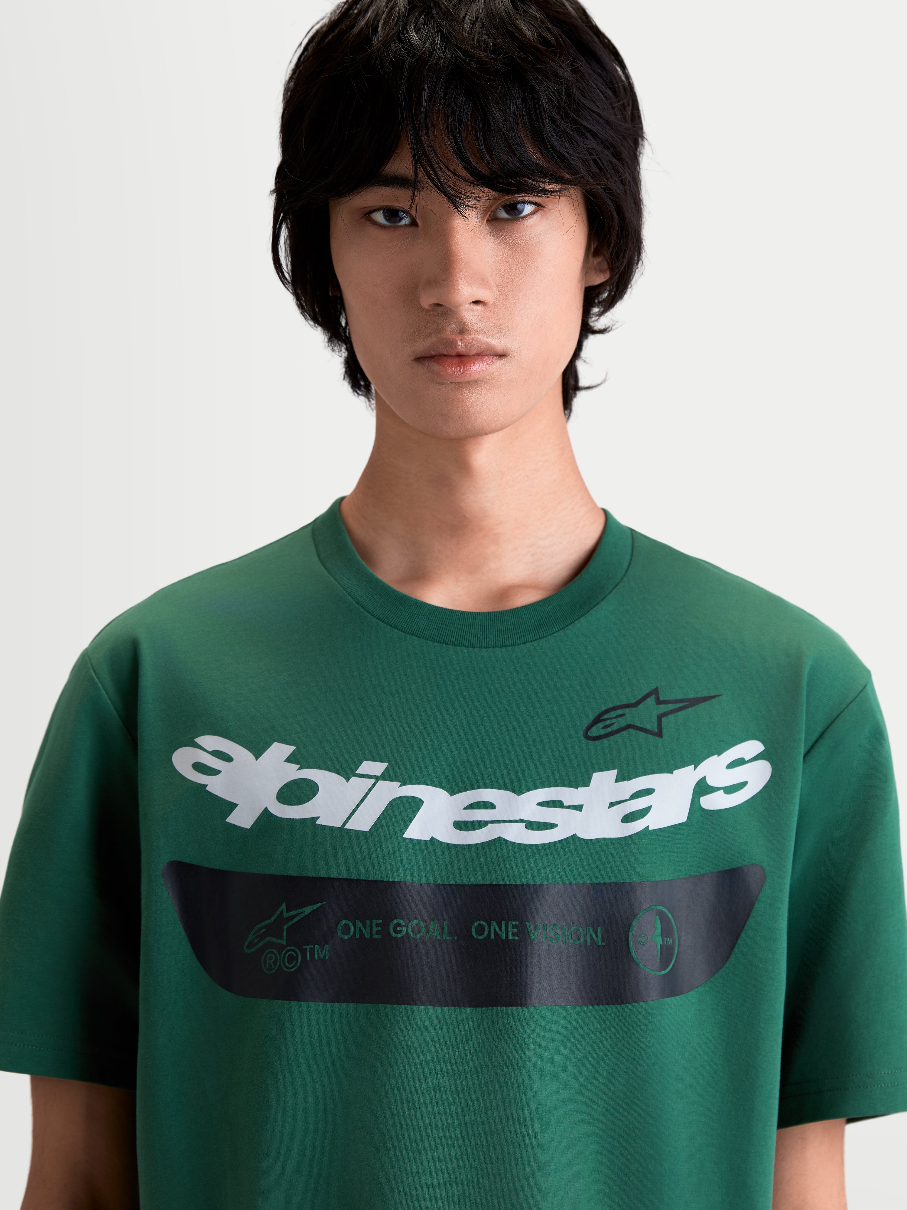 Alpinestars Singular CSF, zielona męska koszulka z krótkim rękawem, odzież sportowa na modelu, biała zakrzywiona grafika z logotypem i czarny pas z mottem One Goal One Vision, komfortowa mieszanka bawełny i poliestru