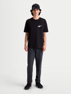 Alpinestars Koszulka Meteor CSF, męski t-shirt z krótkim rękawem, czarny z białym logo Astars na piersi, casualowa odzież sportowa inspirowana motorsportem, model ma na sobie ciemne spodnie i czapkę z daszkiem.