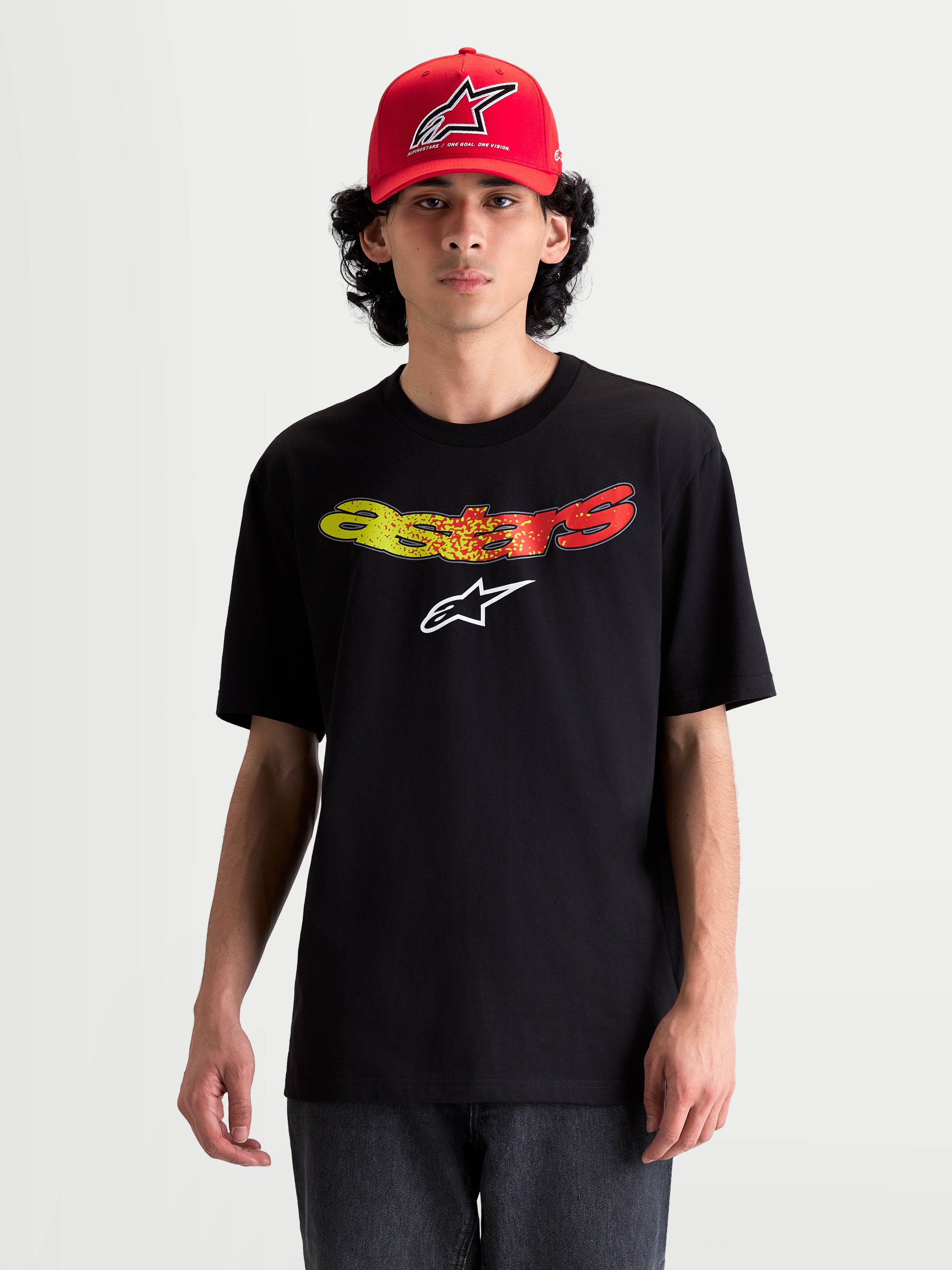 Alpinestars Koszulka Elliptogrit CSF, męska koszulka z krótkim rękawem na modelu, czarna z zakrzywionym logotypem Astars w czerwonym i żółtym gradiencie, miękka mieszanka bawełny i poliestru, casualowa odzież sportowa.