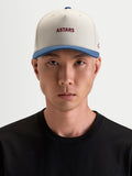 Alpinestars County Canvas Hat, czapka sportswear na modelu, w kolorze piaskowym i niebieskim z haftowanymi logotypami Astars z przodu i z boku, z usztywnioną koroną i zakrzywionym daszkiem