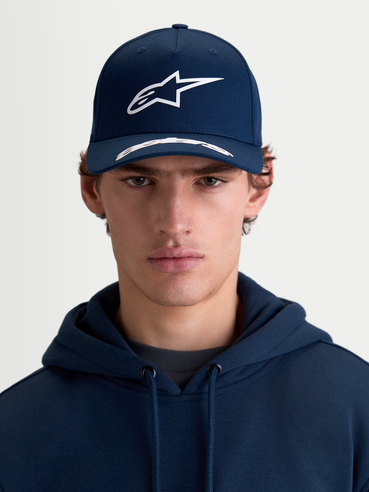 Alpinestars Arclight Hat, Sportswear Curved Bill Cap, Navy Blue and White, Front View on Model, featuring a Structured Crown, Textured Puff Print Astars Logo, and Premium Cotton Twill.