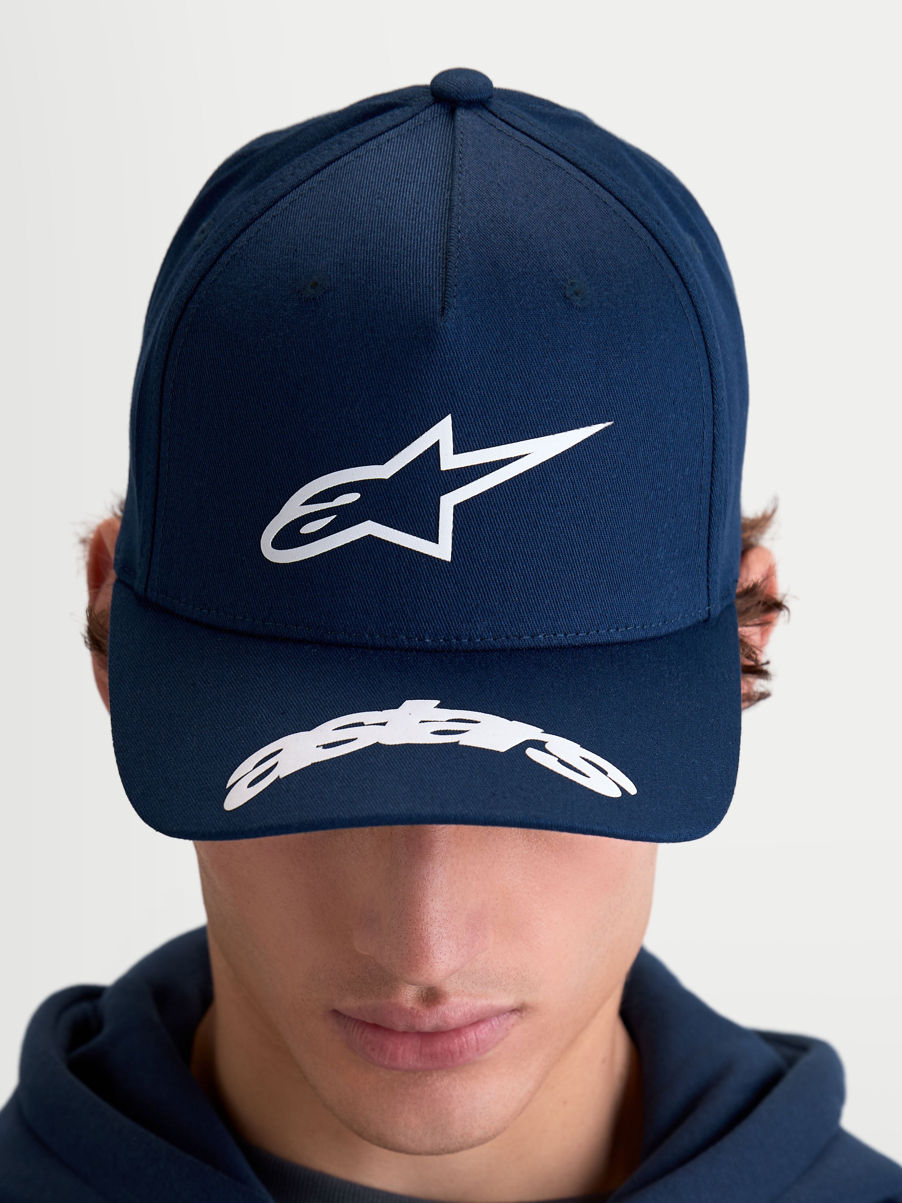 Alpinestars Arclight Hat, czapka z daszkiem sportswear inspirowana motorsportem, dla kobiet i mężczyzn, granatowa i biała, usztywniona korona z teksturowanym logo Astars puff-print, zakrzywiony daszek z logotypem Astars, trwała bawełniana tkanina keprowa, widok z przodu na modelu.