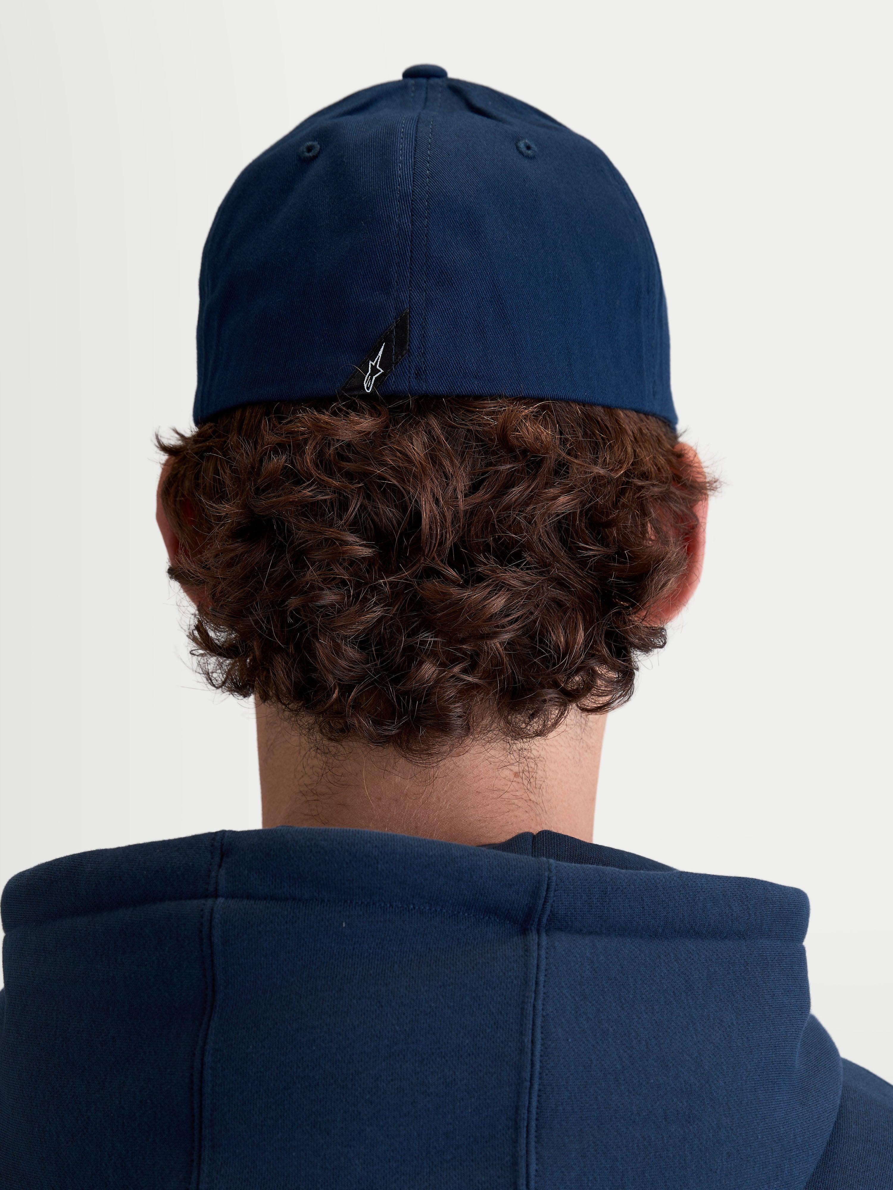 Alpinestars Arclight Hat, granatowa czapka z daszkiem, sportowa odzież unisex, wytrzymała tkanina keprowa, elastyczny tył flex back, widok z tyłu na modelu z widoczną metką z logo Astars.