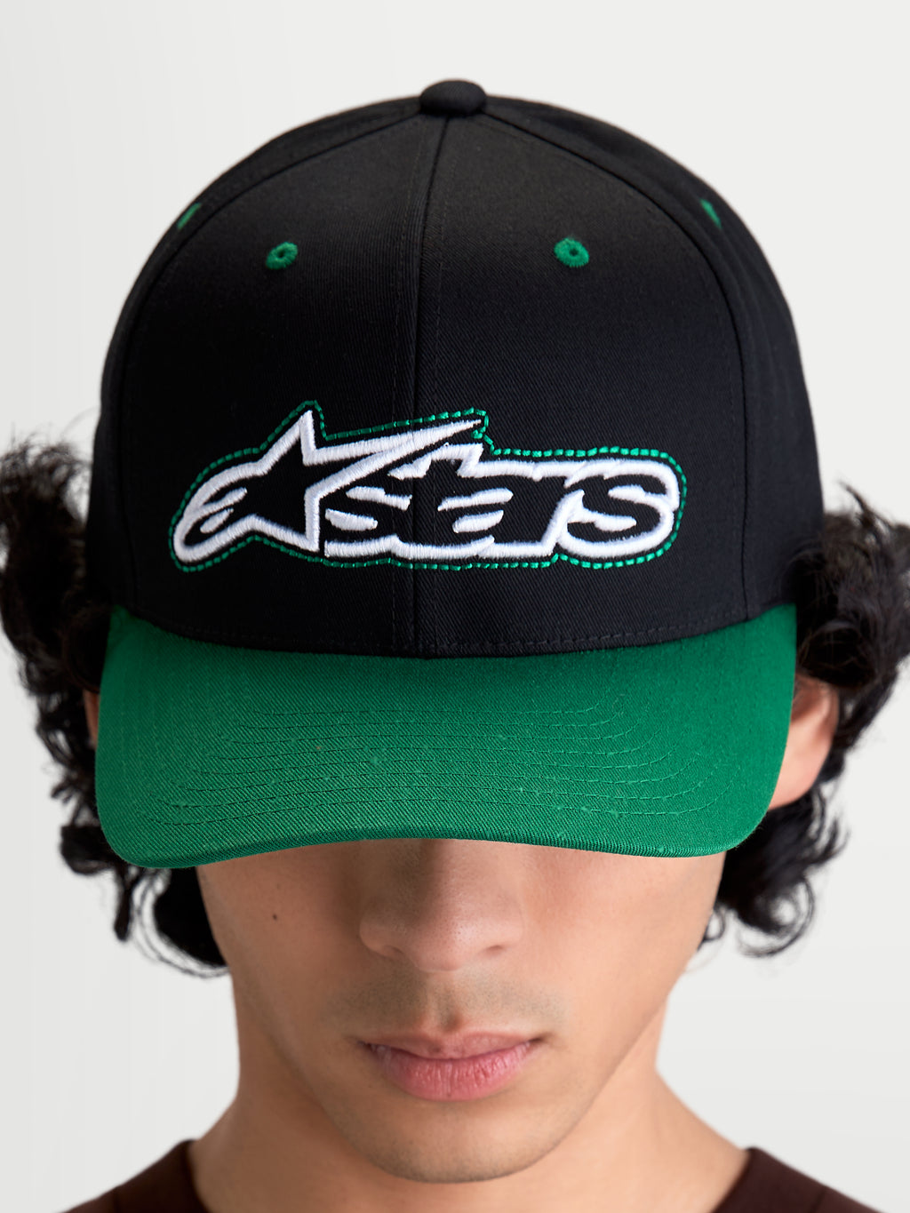 Alpinestars Retro Snapback Hat, Motorsport-inspired sportswear baseball cap with curved bill and structured crown, Unisex, Black and Green, Cotton Twill, front view on model showing the Astars logo with green pop-color running stitch detailing.