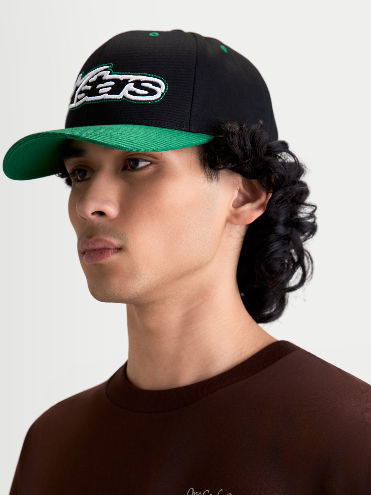 Alpinestars Czapka Retro Snapback, męska czapka sportswear noszona przez modela, czarna i zielona, usztywniona korona, zakrzywiony daszek, haftowane logo Astars z zielonym ściegiem, konstrukcja z bawełnianego kepru.